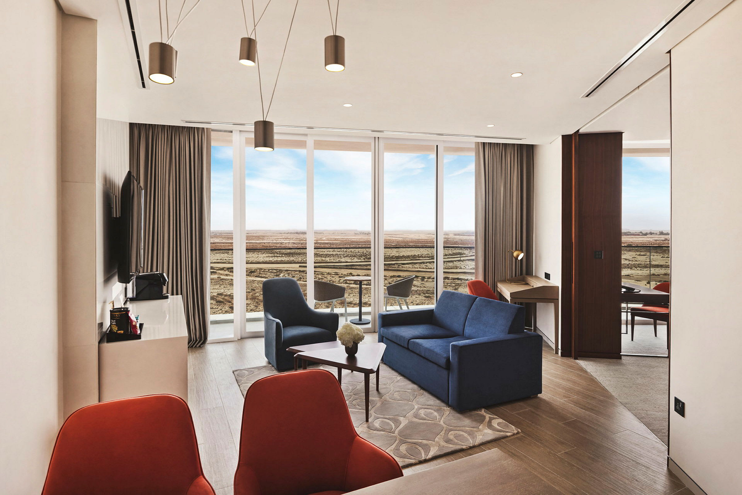 Ett modernt hotellrum med en sittgrupp, stora fönster som vetter mot en öppen landskap och ett skrivbord. (AI-genererad text)