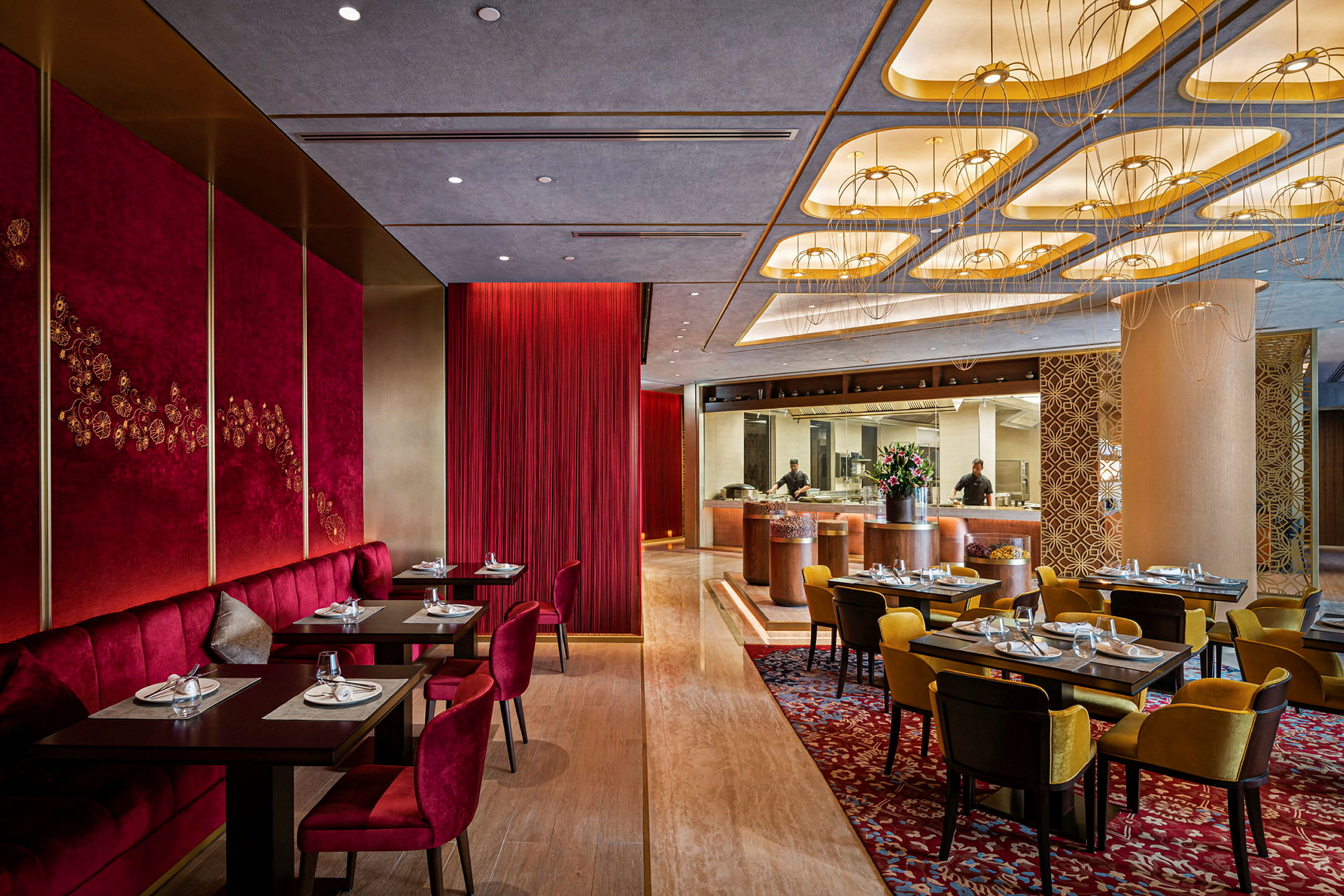En elegant restaurang med röda och gula sittplatser, vakert dekorerade tak och ett öppet kök. (AI-genererad text)