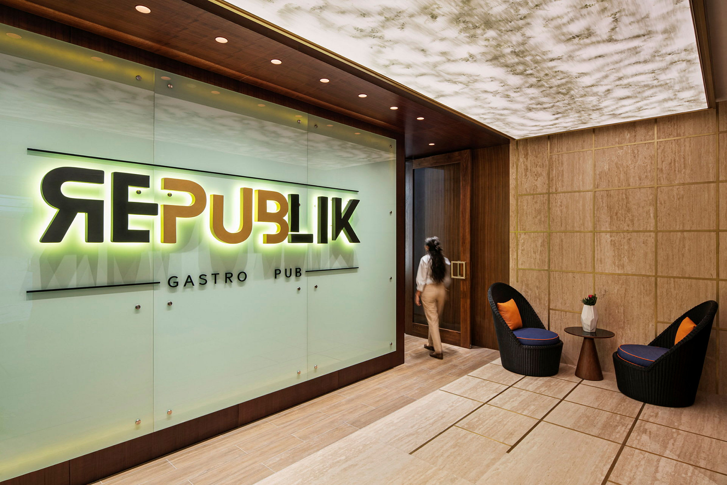 Entrén till en restaurang eller bar med en skylt som lyder "Republik Gastro Pub". I förgrunden syns två stolar och ett bord. (AI-genererad text)