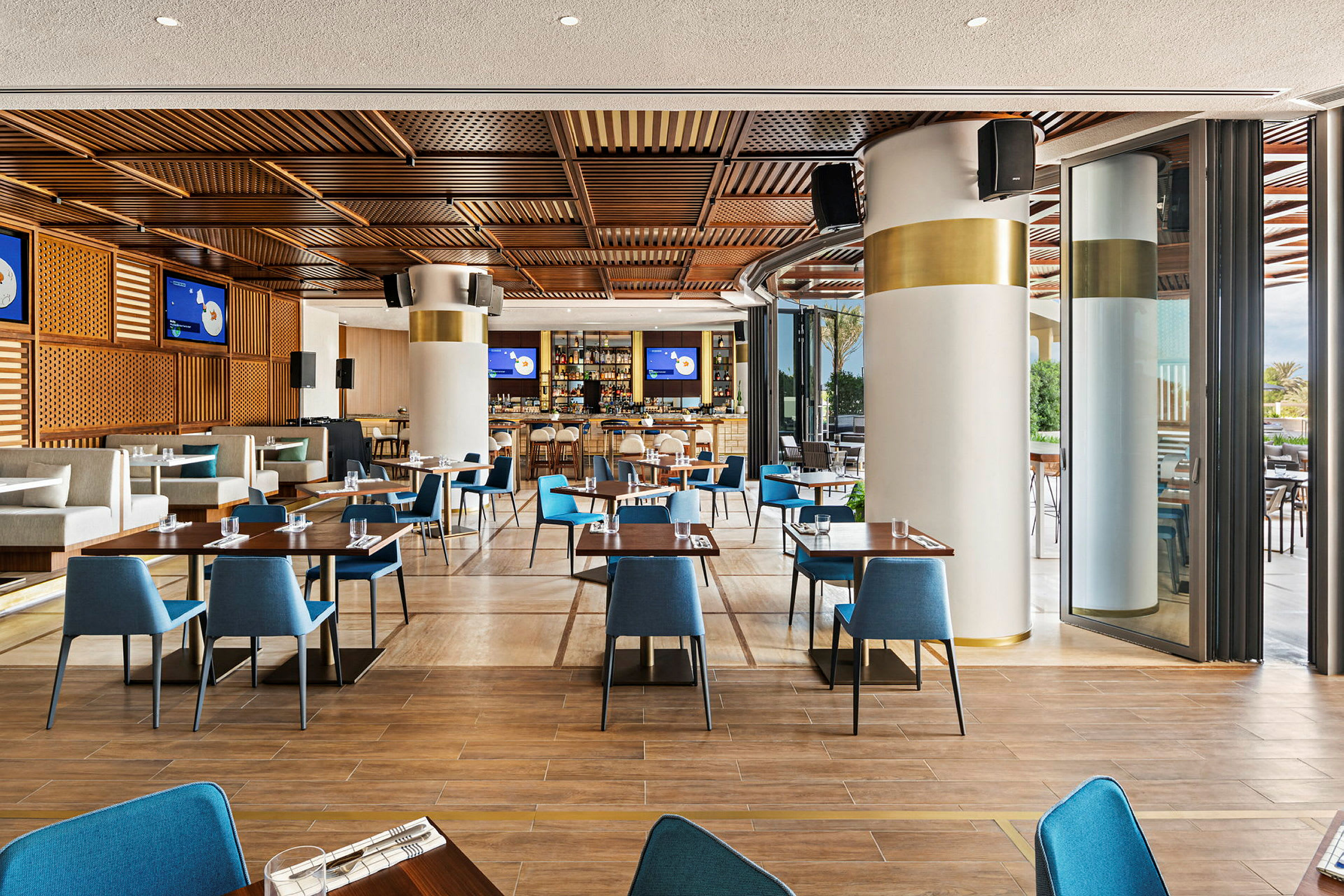 En modern restaurang med trädetaljer i taket, blå stolar och dukade bord. (AI-genererad text)