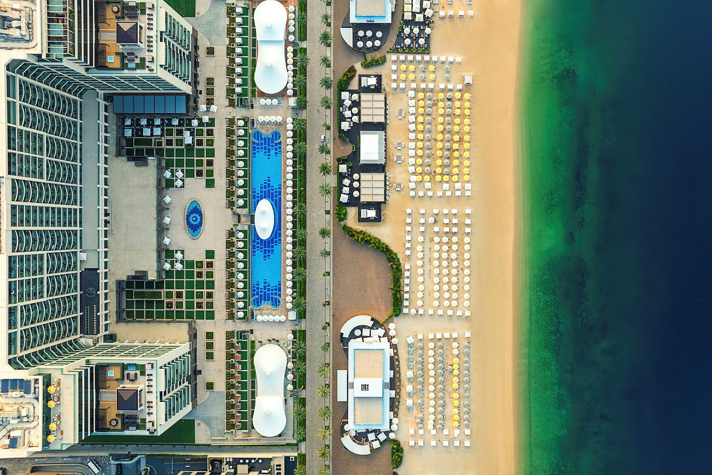 Luftvy av hotellområde med pooler och solstolar bredvid strand och hav. (AI-genererad text)