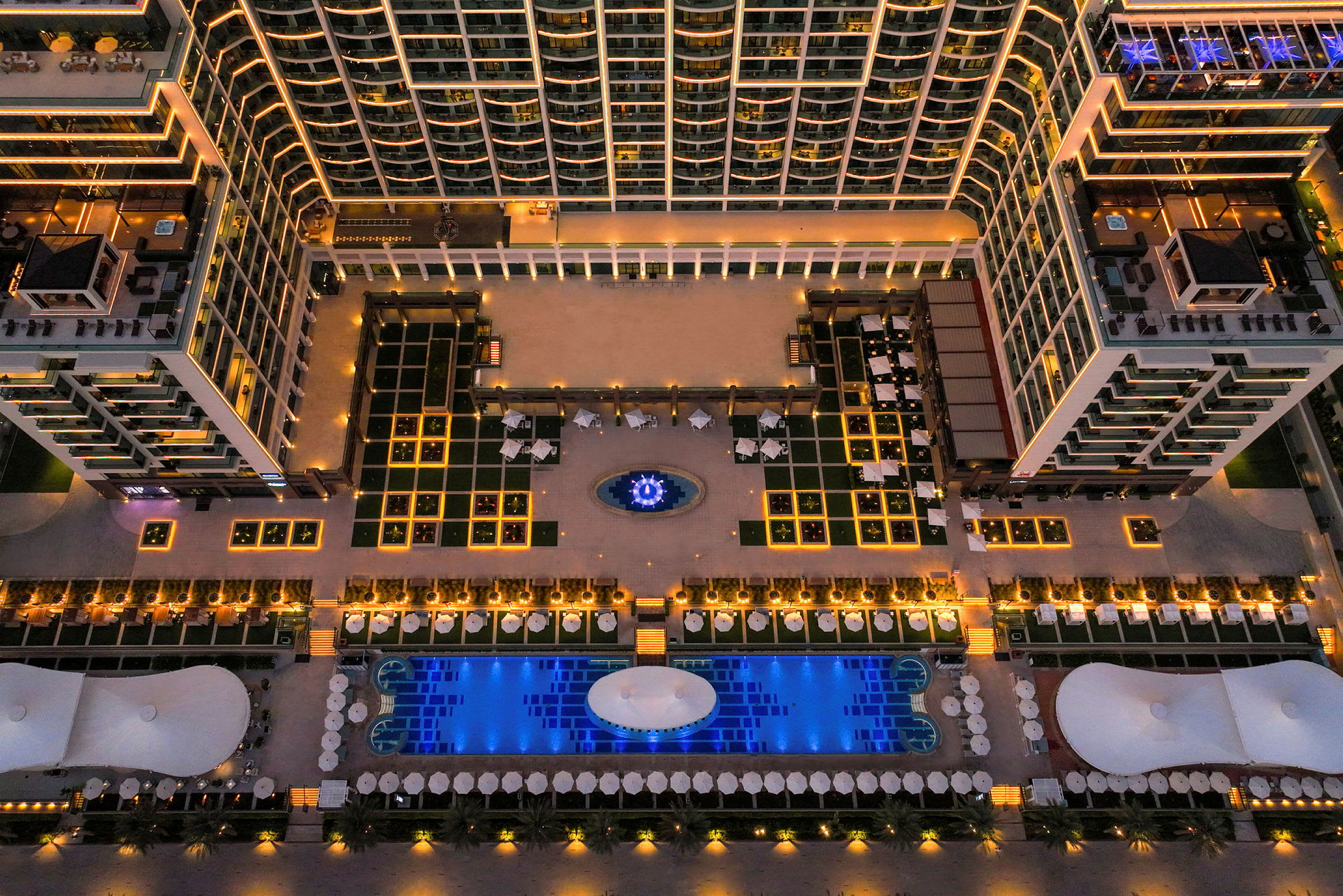 Flygbild över en hotellanläggning med upplysta byggnader och en pool. (AI-genererad text)