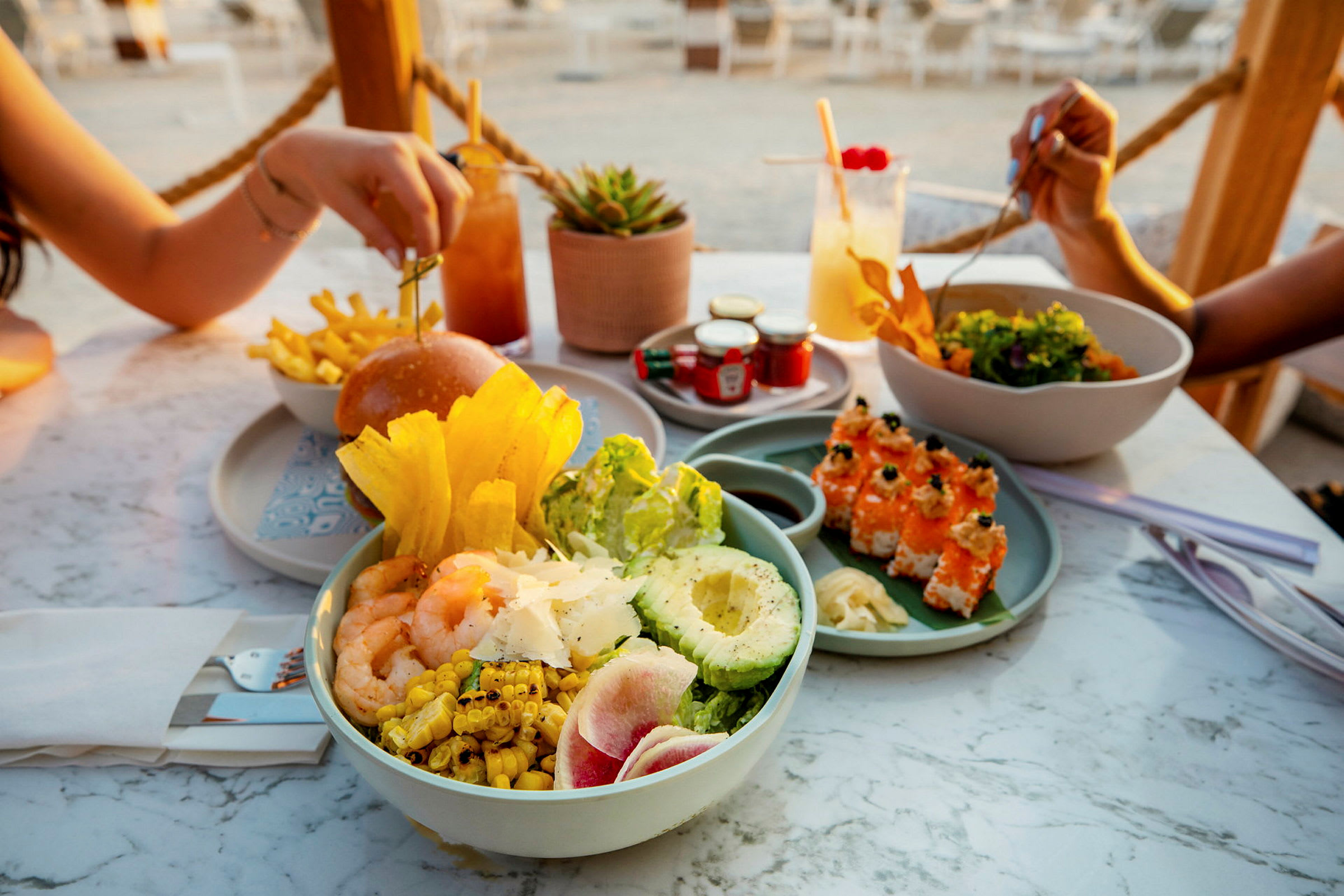 En bord fylld med olika maträtter inklusive sallad, sushi, hamburger och drycker. (AI-genererad text)