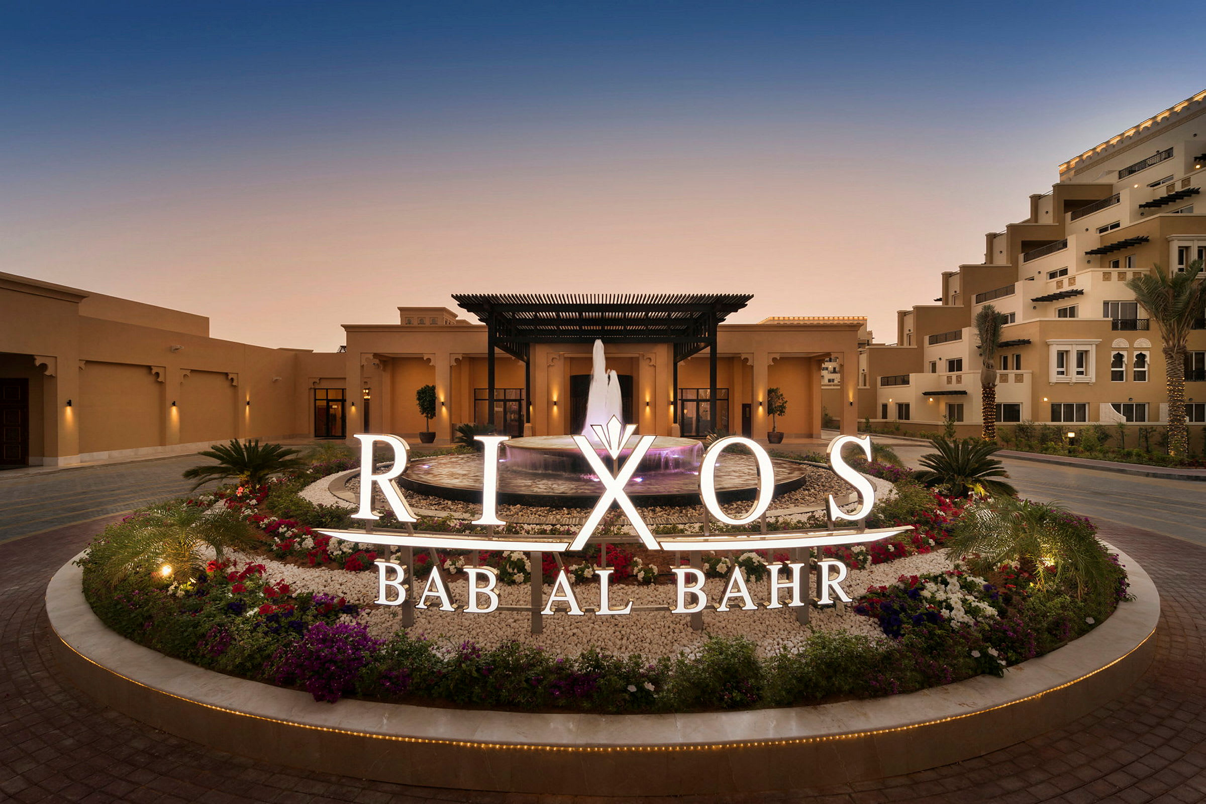 Hotellentré med fontän och omgivande blommor, skylt med texten Rixos Bab Al Bahr. (AI-genererad text)