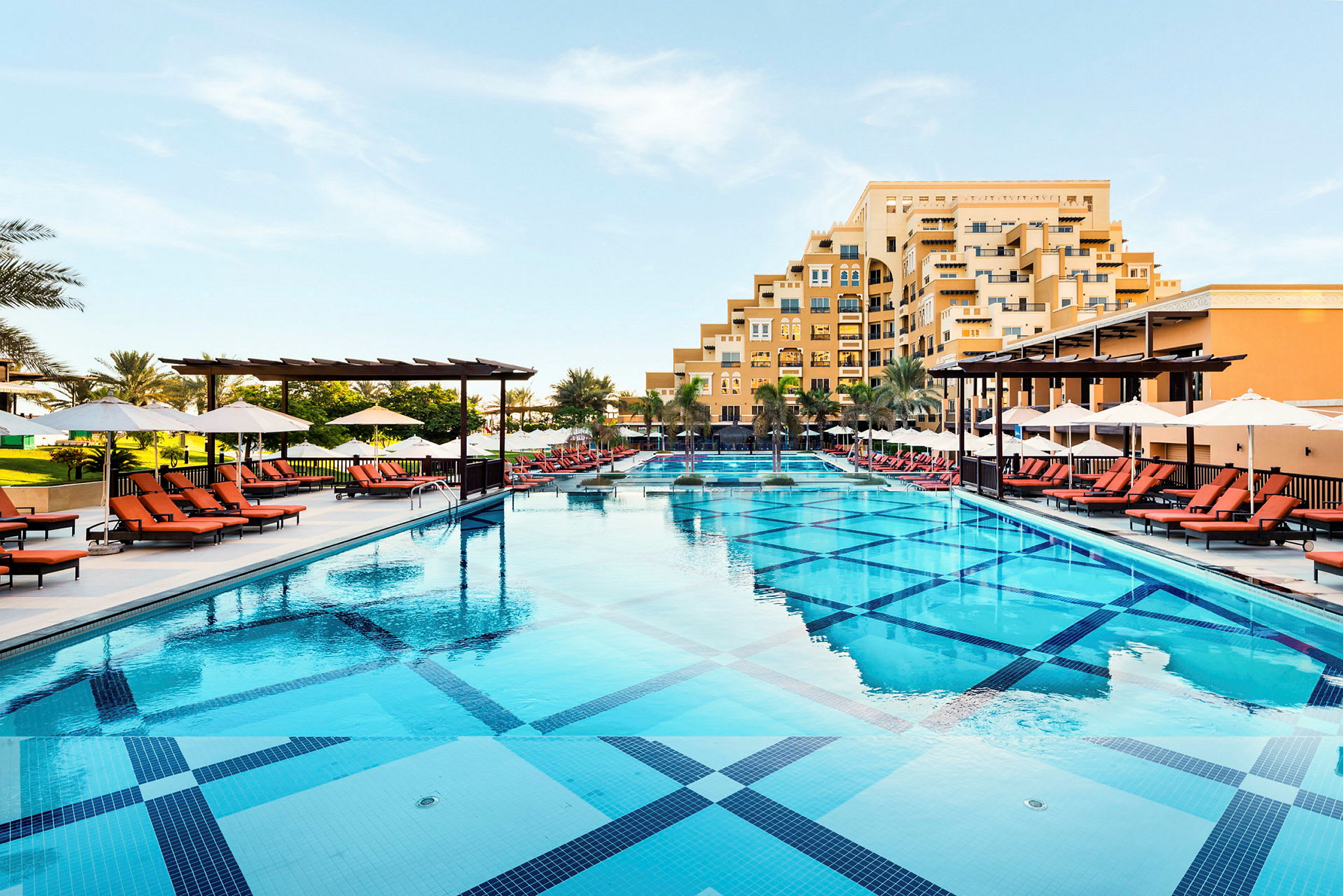 En stor swimmingpool med solstolar och parasoller vid sidan av ett hotell. (AI-genererad text)