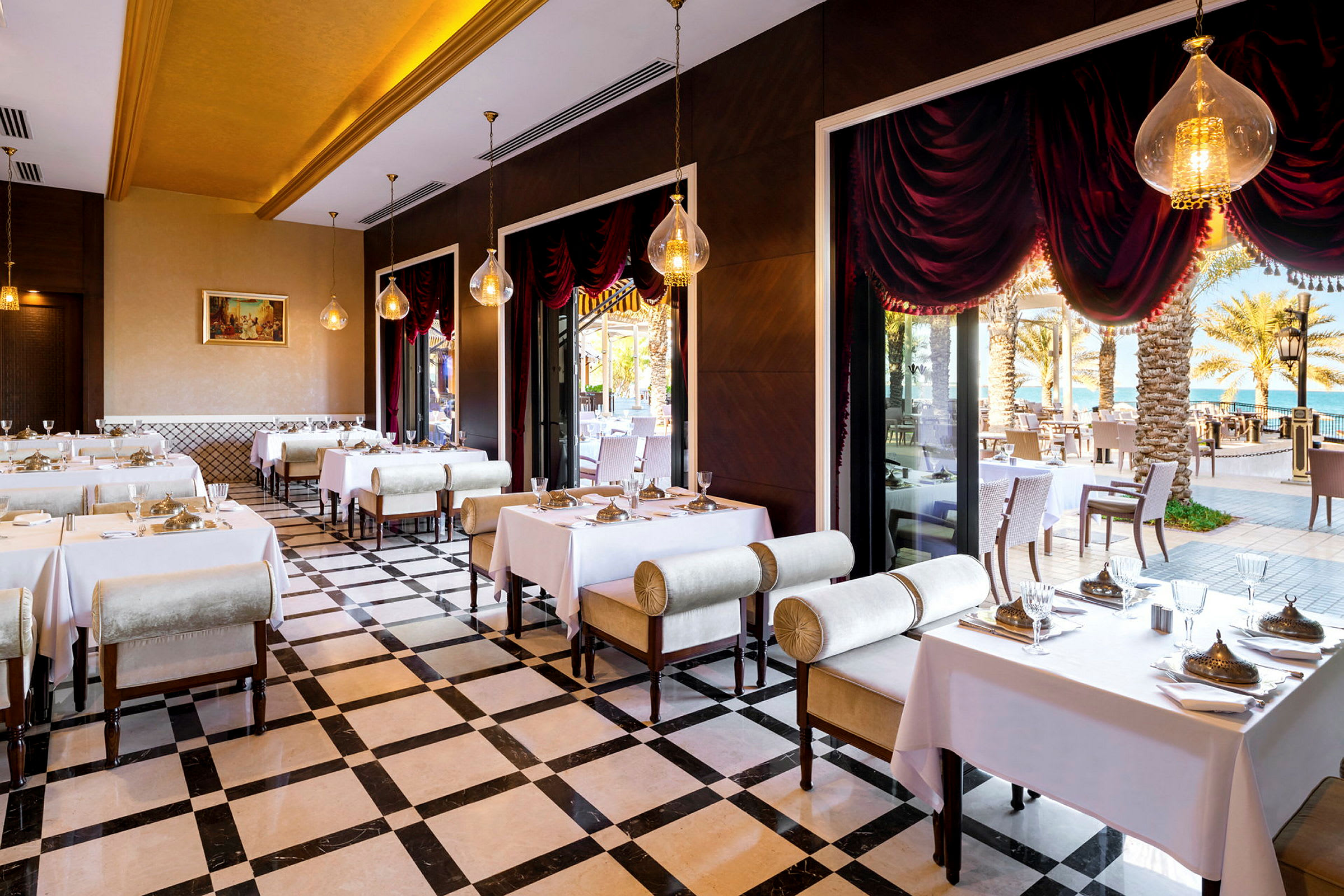 En elegant restaurang med dukade bord, stora fönster och vy mot palmer och hav. (AI-genererad text)
