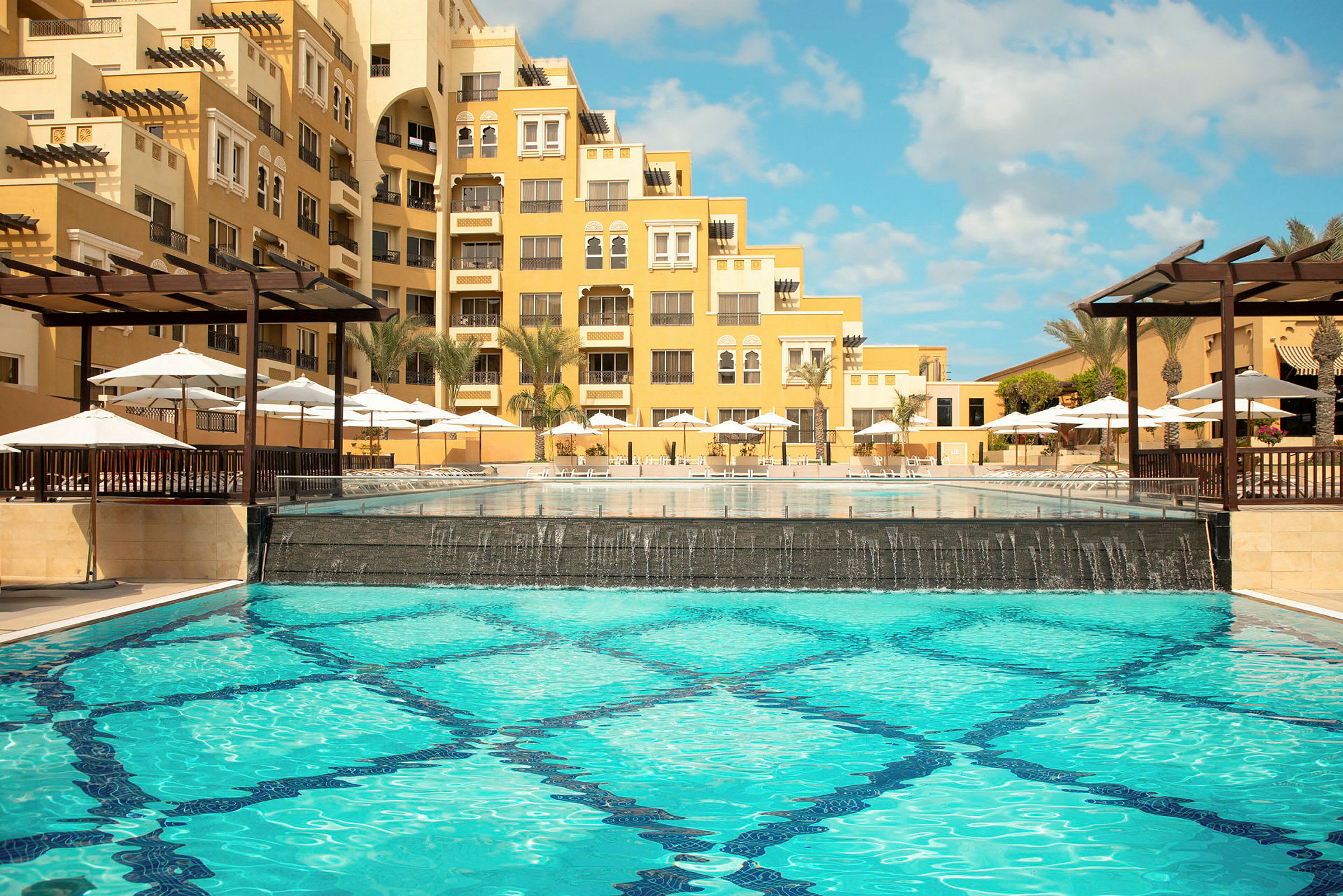 Ett hotell med gul fasad, pool och parasoller. (AI-genererad text)