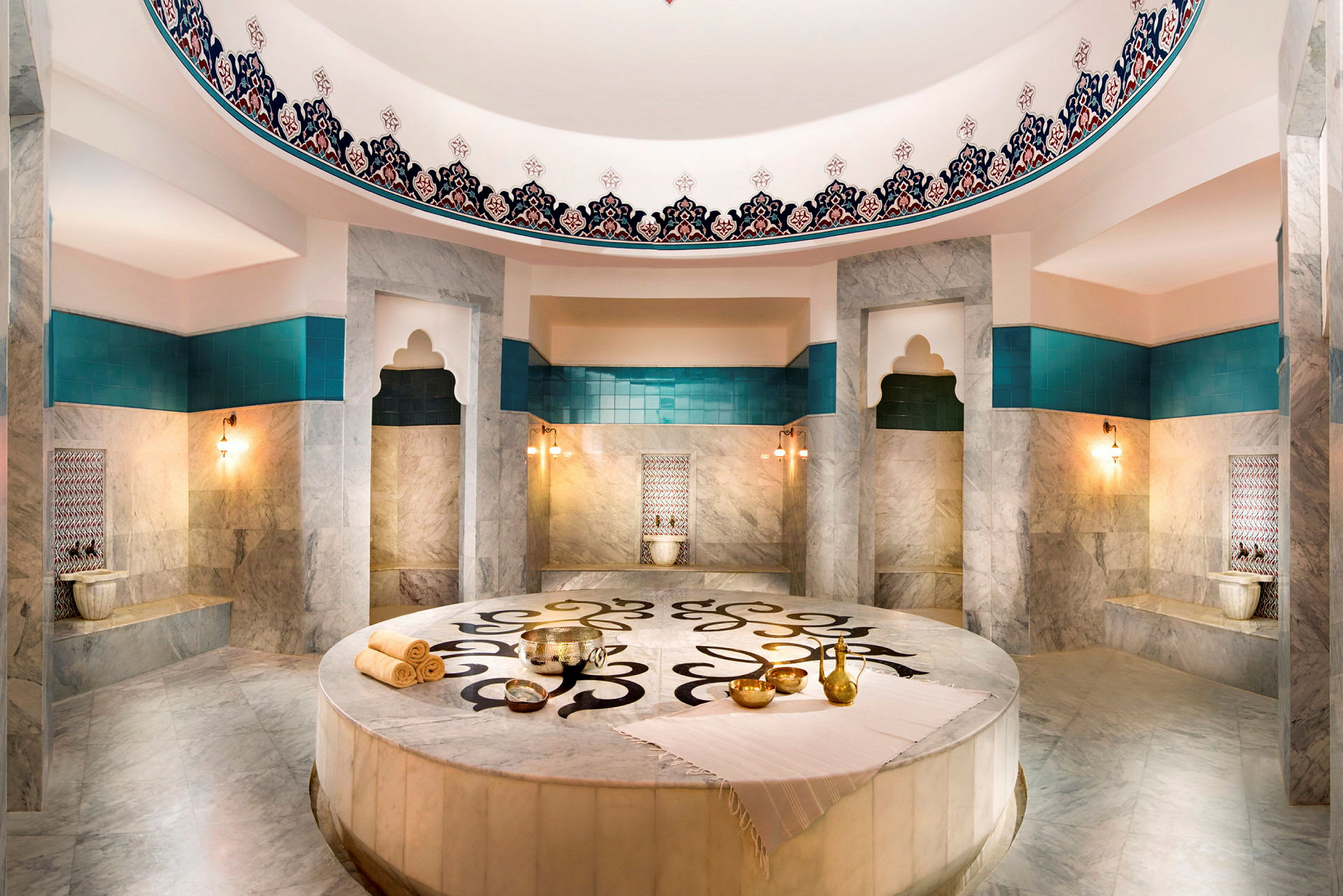 Ett rum i en hamam med marmorytor, turkosa detaljer och dekorationer. (AI-genererad text)