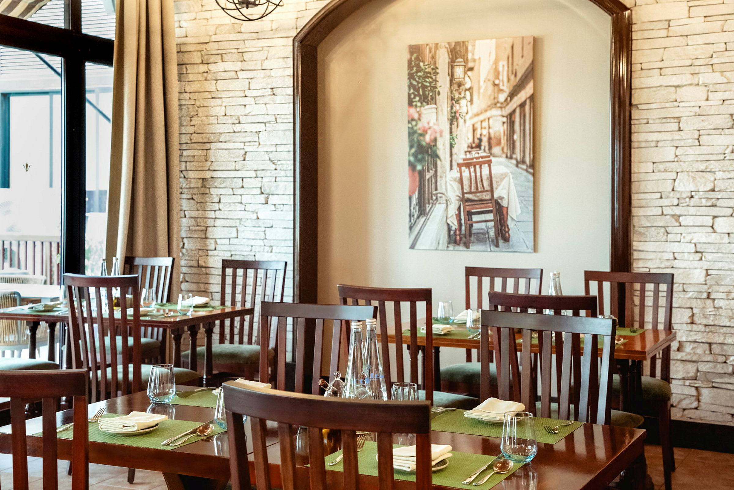 Interiören av en restaurang med trämöbler och dukade bord, med en bild på väggen av en gata. (AI-genererad text)