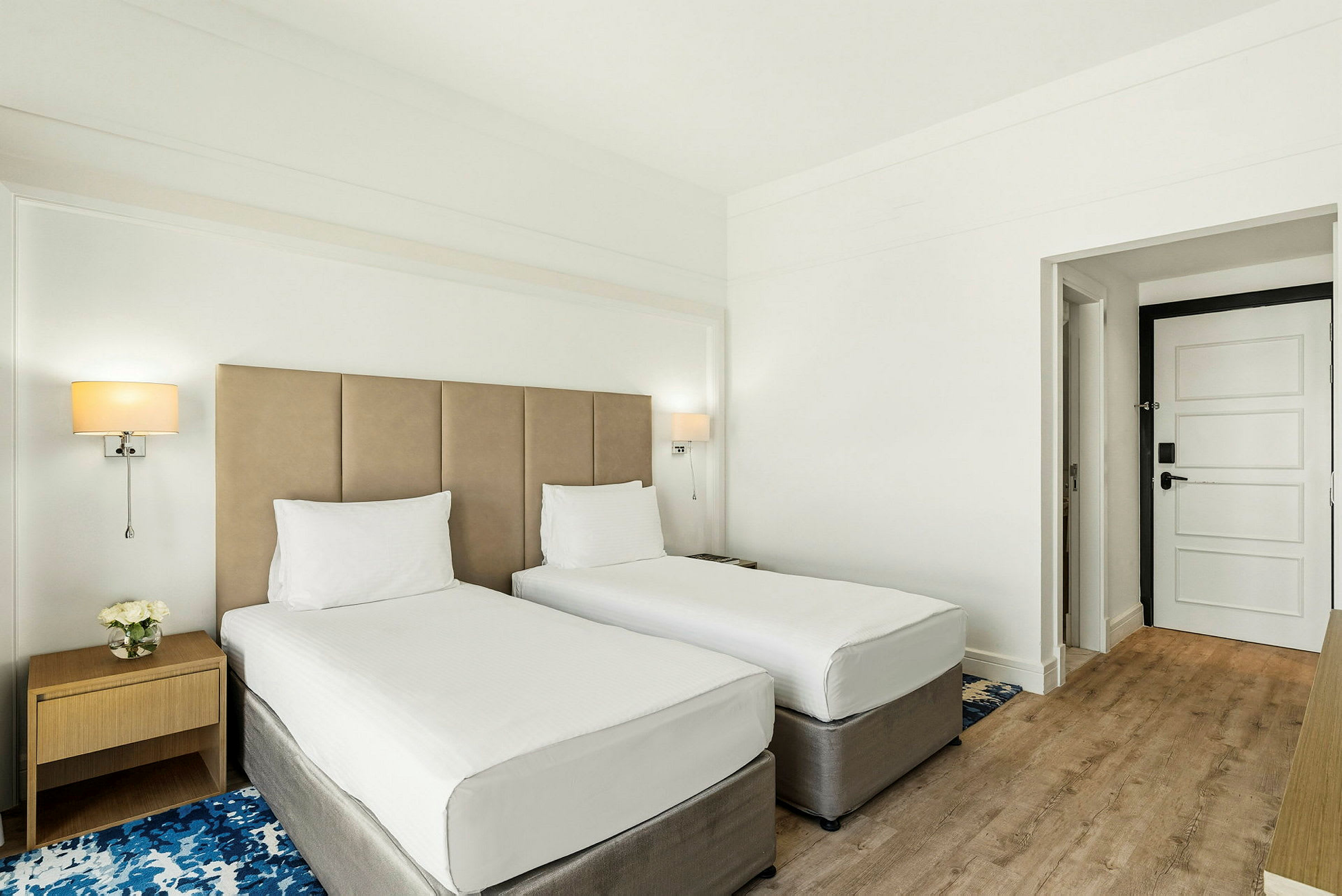 Ett hotellrum med två enkelsängar, ett nattduksbord och en dörr. (AI-genererad text)