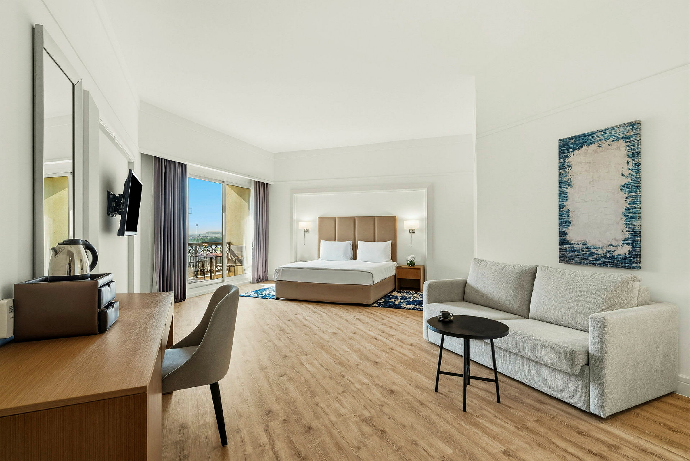 Hotellets rum med en dubbelsäng, en soffa och ett skrivbord, samt en balkong med utsikt. (AI-genererad text)