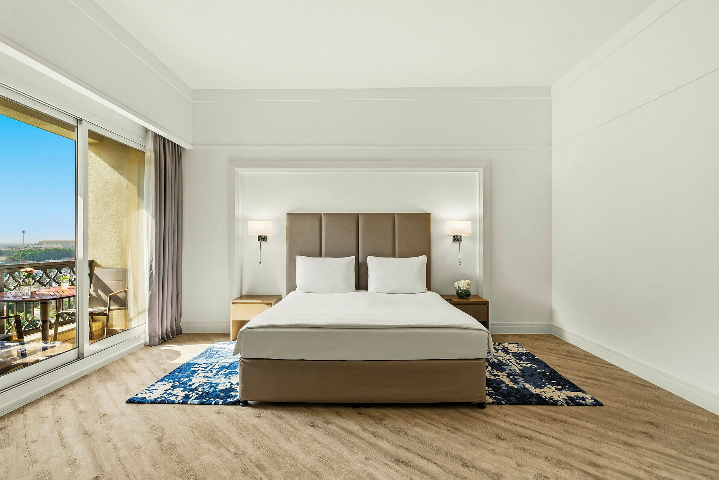 Ett hotellrum med en stor säng, två sängbord och en balkong med utsikt. (AI-genererad text)