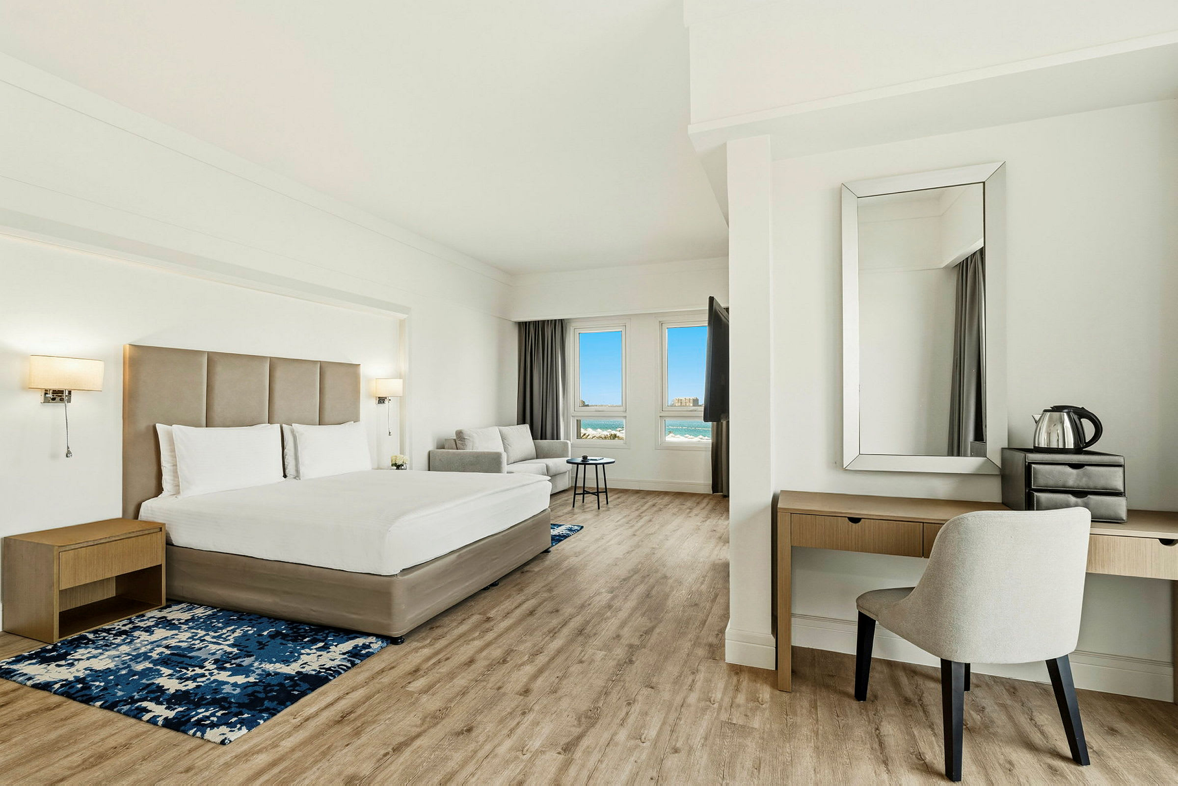 Modernt hotellrum med en dubbelsäng, sittgrupp och utsikt mot havet genom fönstren. (AI-genererad text)