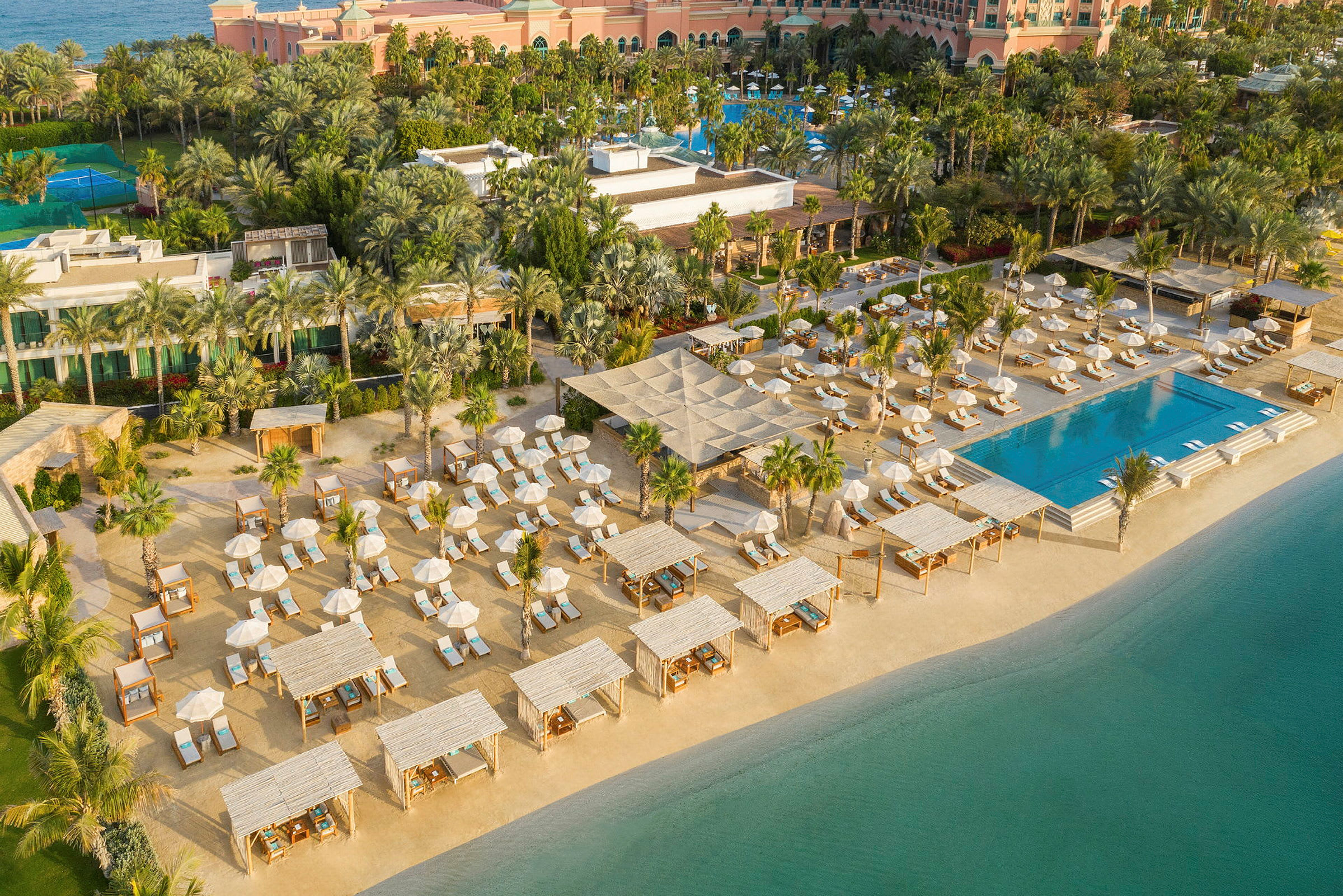 Flygbild av en resort med pool, solstolar och parasoller vid stranden. (AI-genererad text)
