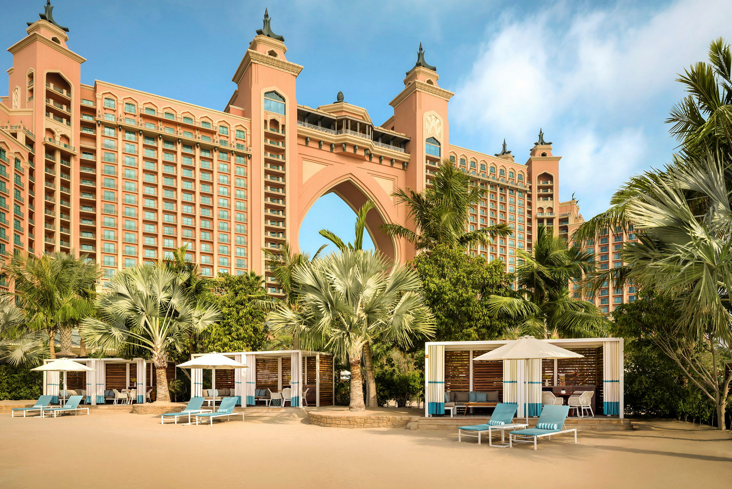 En storslagen hotellbyggnad med bågformad arkitektur, omgiven av palmer och strandhytter. (AI-genererad text)