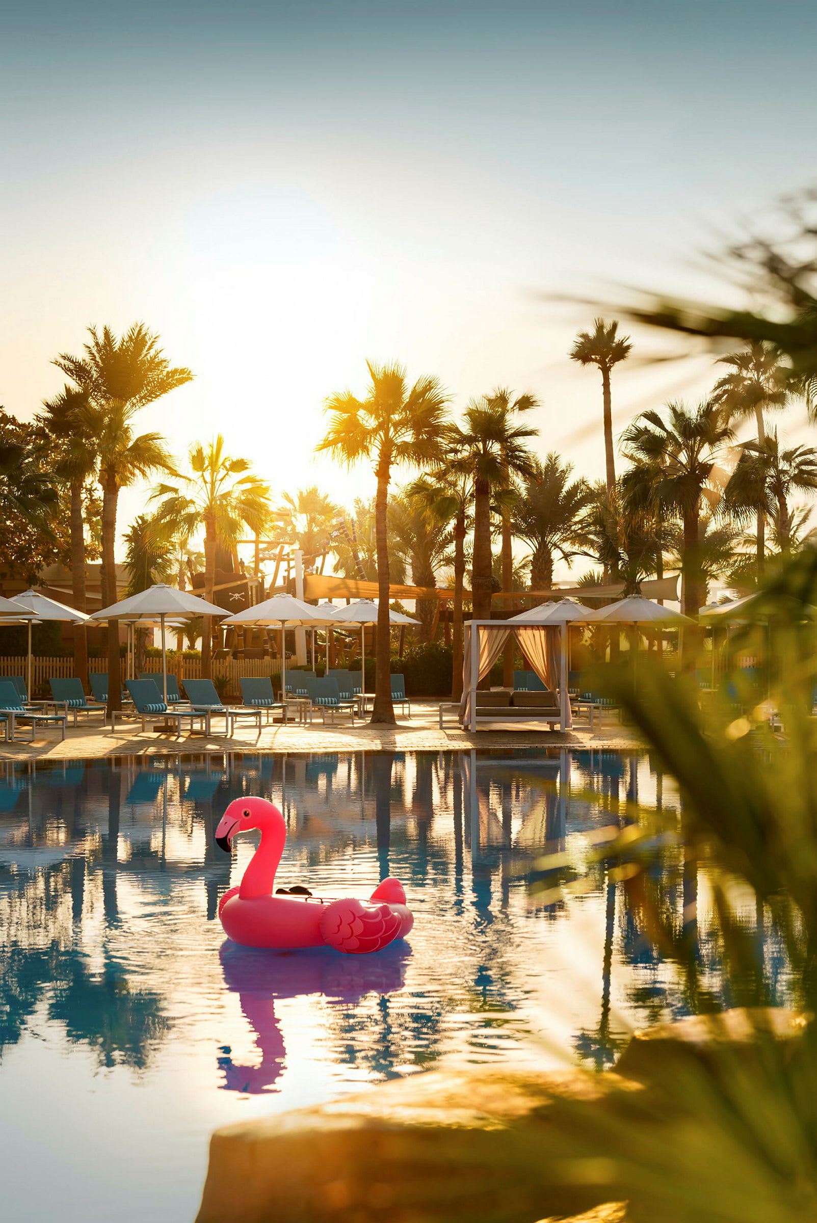 Rosa uppblåsbar flamingo i hotellpool med palmer och solstolar i bakgrunden. (AI-genererad text)