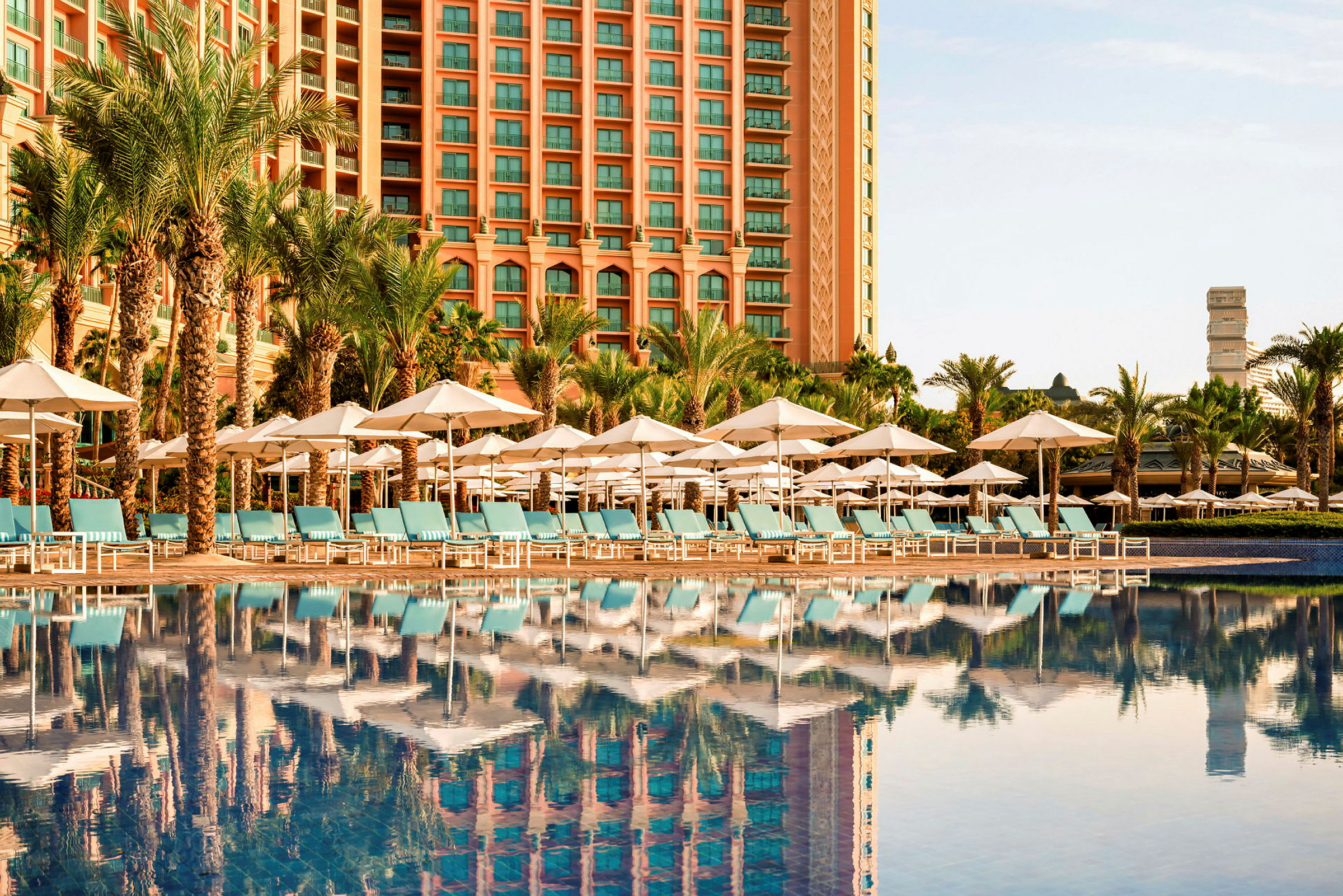En hotellfasad med en rad solstolar och parasoller vid en pool. (AI-genererad text)