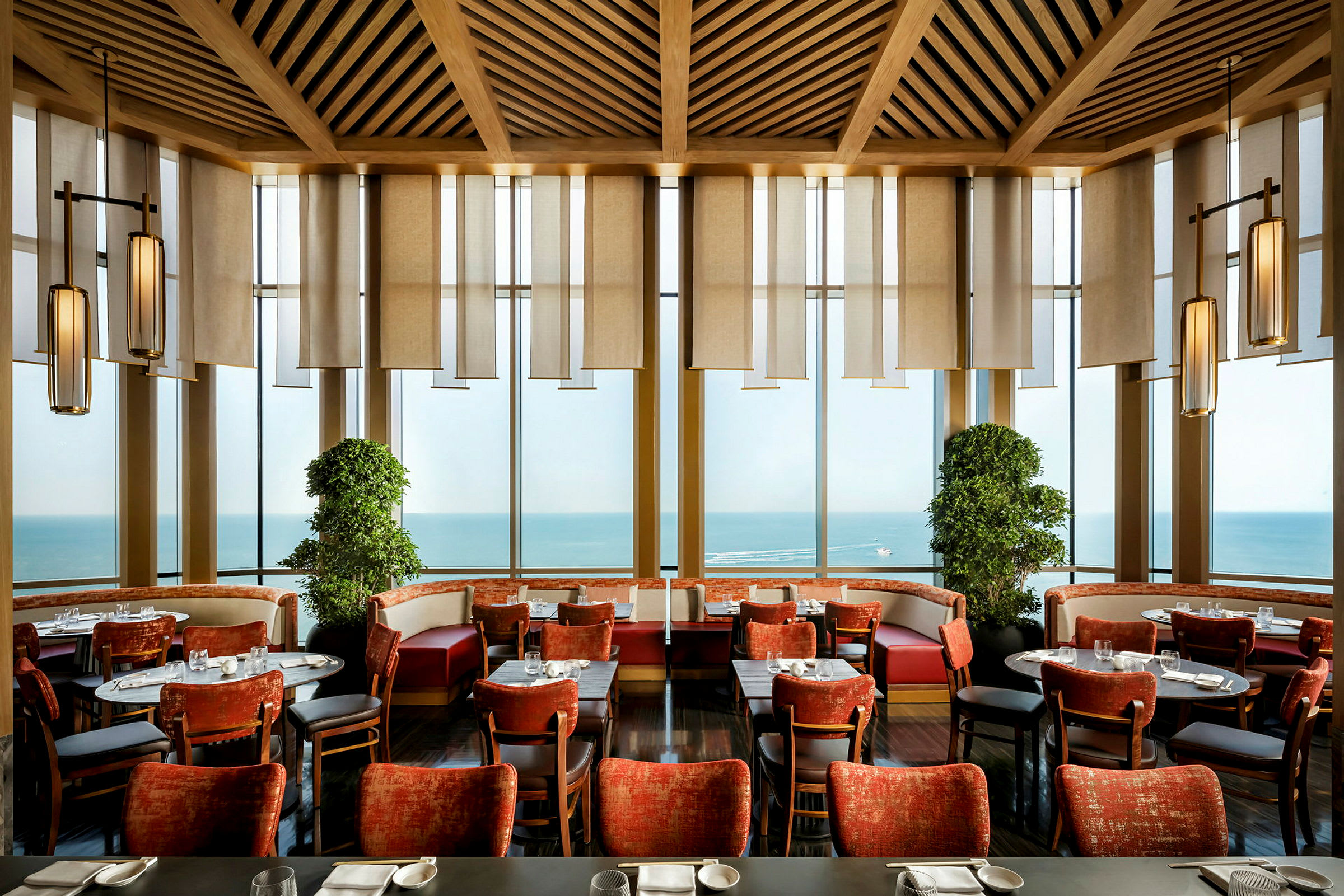 Interiör av en restaurangs matsal med röda stolar, panoramafönster och havsutsikt. (AI-genererad text)
