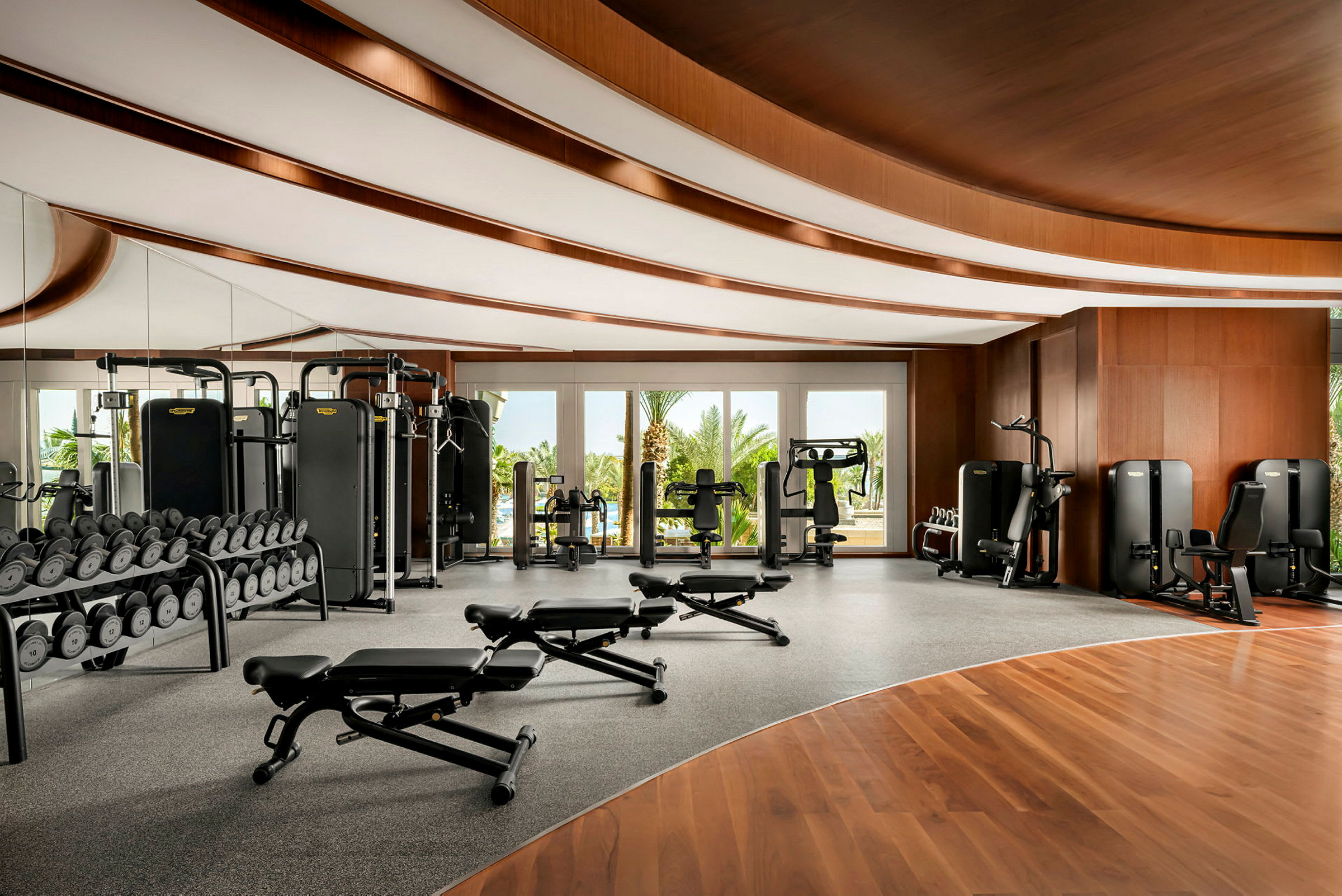 Bild av ett gym med träningsutrustning och utsikt över gröna träd genom glasfönster. (AI-genererad text)