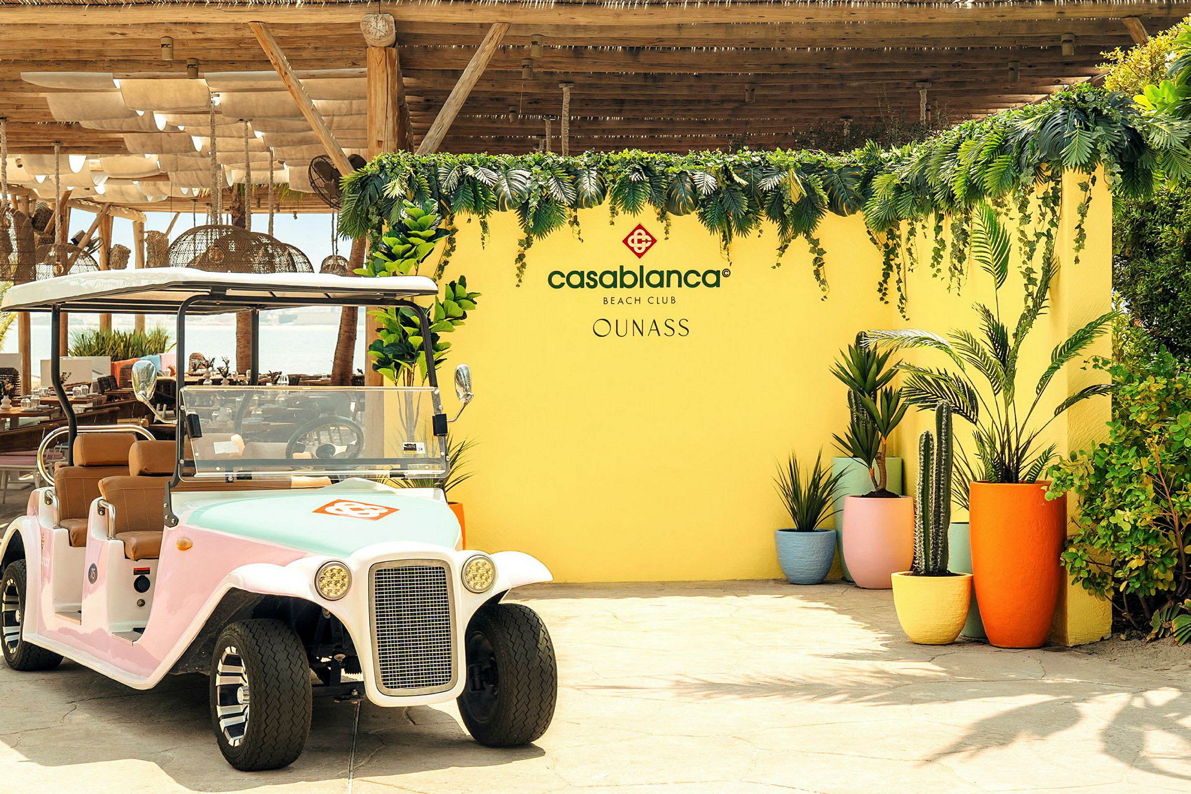 En golfbil står framför en gul vägg dekorerad med växtlighet och blommor samt texten 'Casablanca Beach Club'. (AI-genererad text)