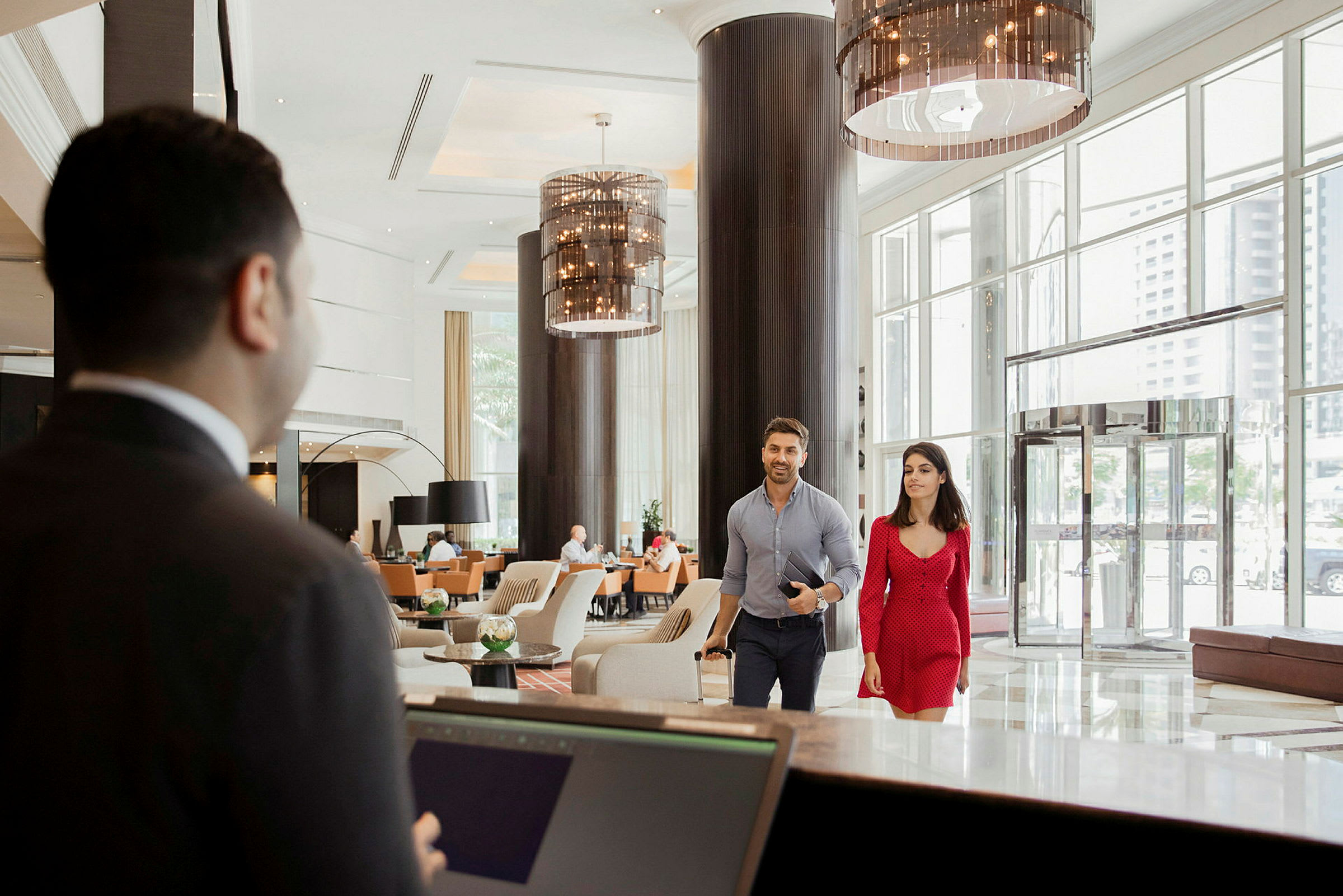 Interiör av en hotellobby med en reception i förgrunden och två gäster som går mot receptionen. (AI-genererad text)