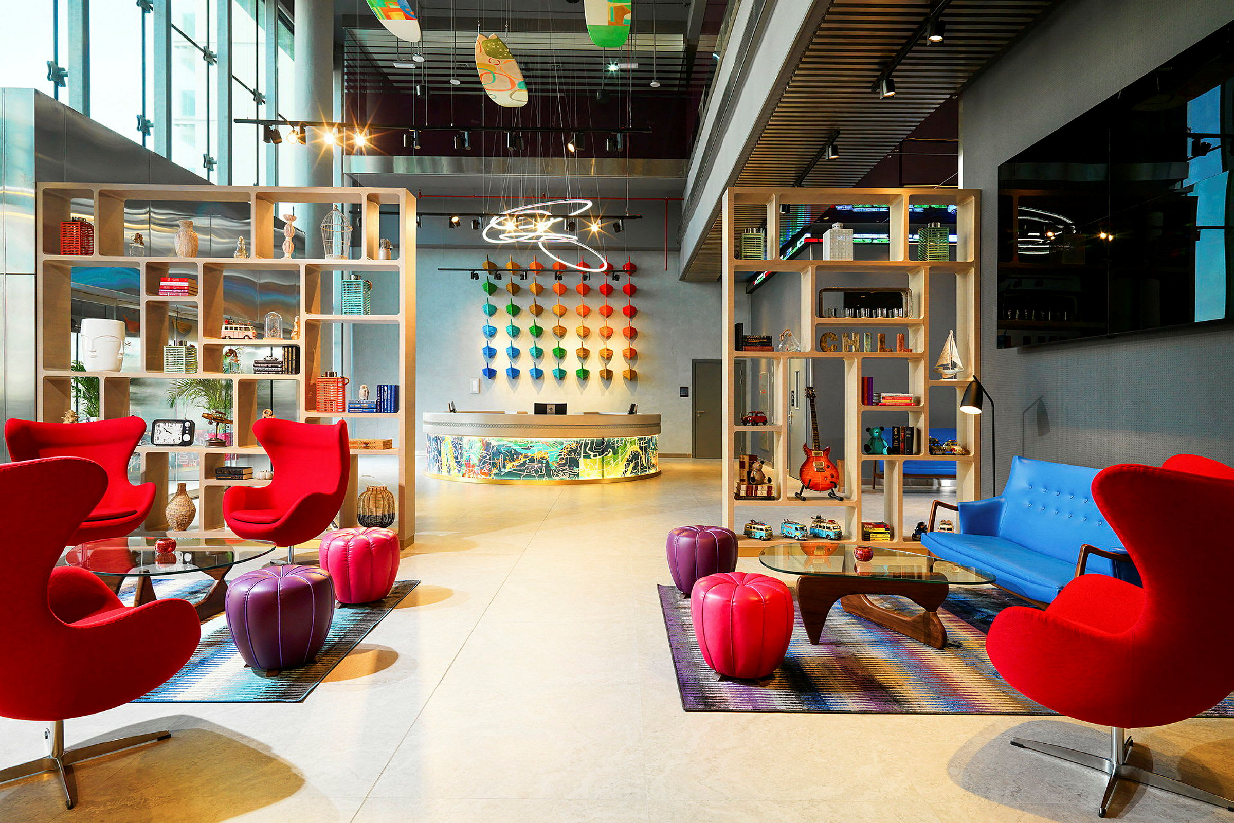 En modern och färgglad hotellobby med röda stolar, ett blått soffmöblemang och hyllor fyllda med dekorativa föremål. (AI-genererad text)