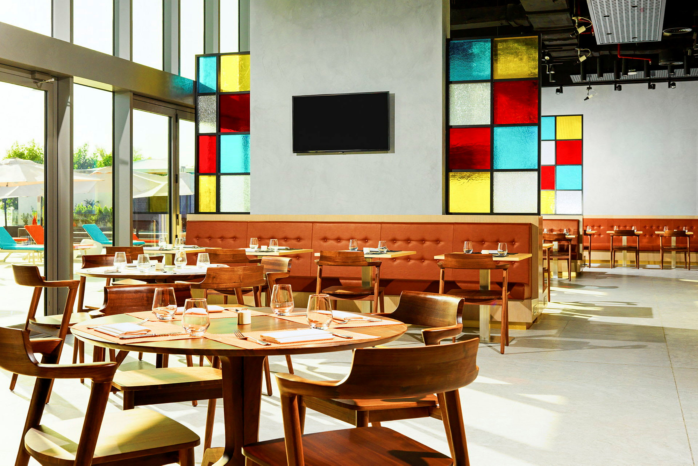 Bild av en modern restaurang med färgglada glaspaneler och träbord, uppdukat för gäster. (AI-genererad text)