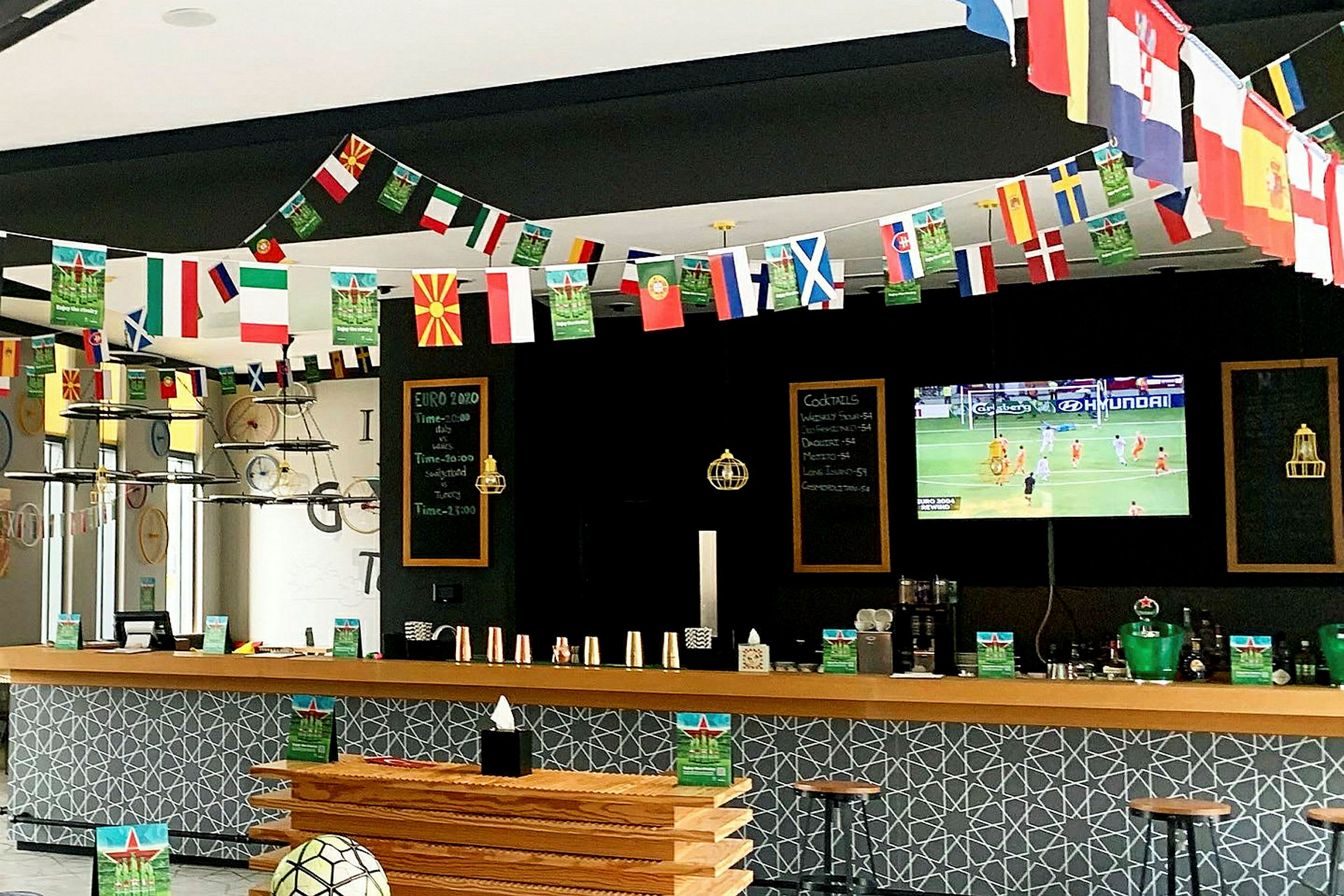 En sportbar med dekorationer av landsflaggor och en TV som visar en fotbollsmatch. (AI-genererad text)