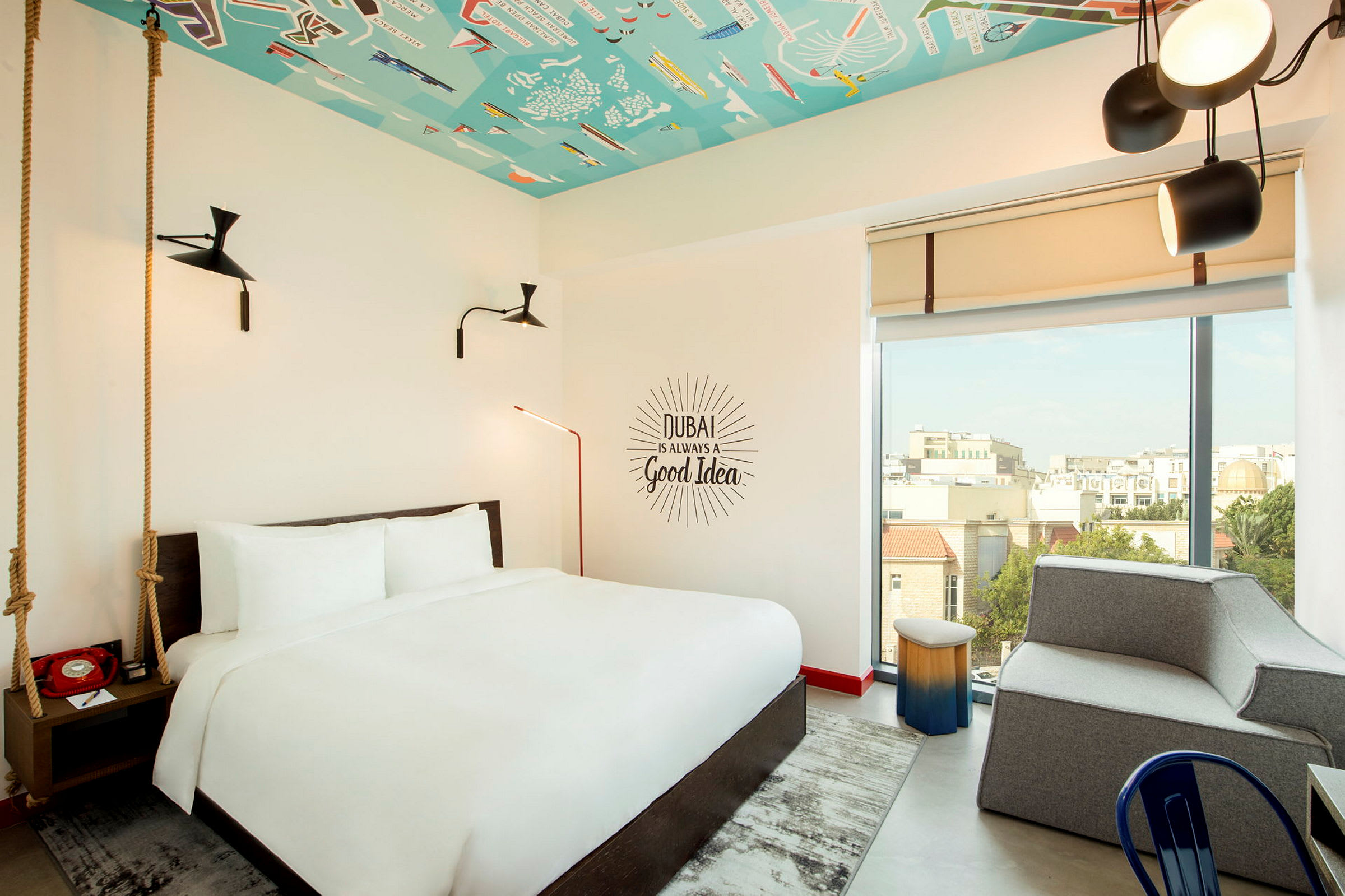 Ett hotellrum med en stor säng, modern inredning och ett färgglatt tak. Ett stort fönster ger utsikt över staden. (AI-genererad text)