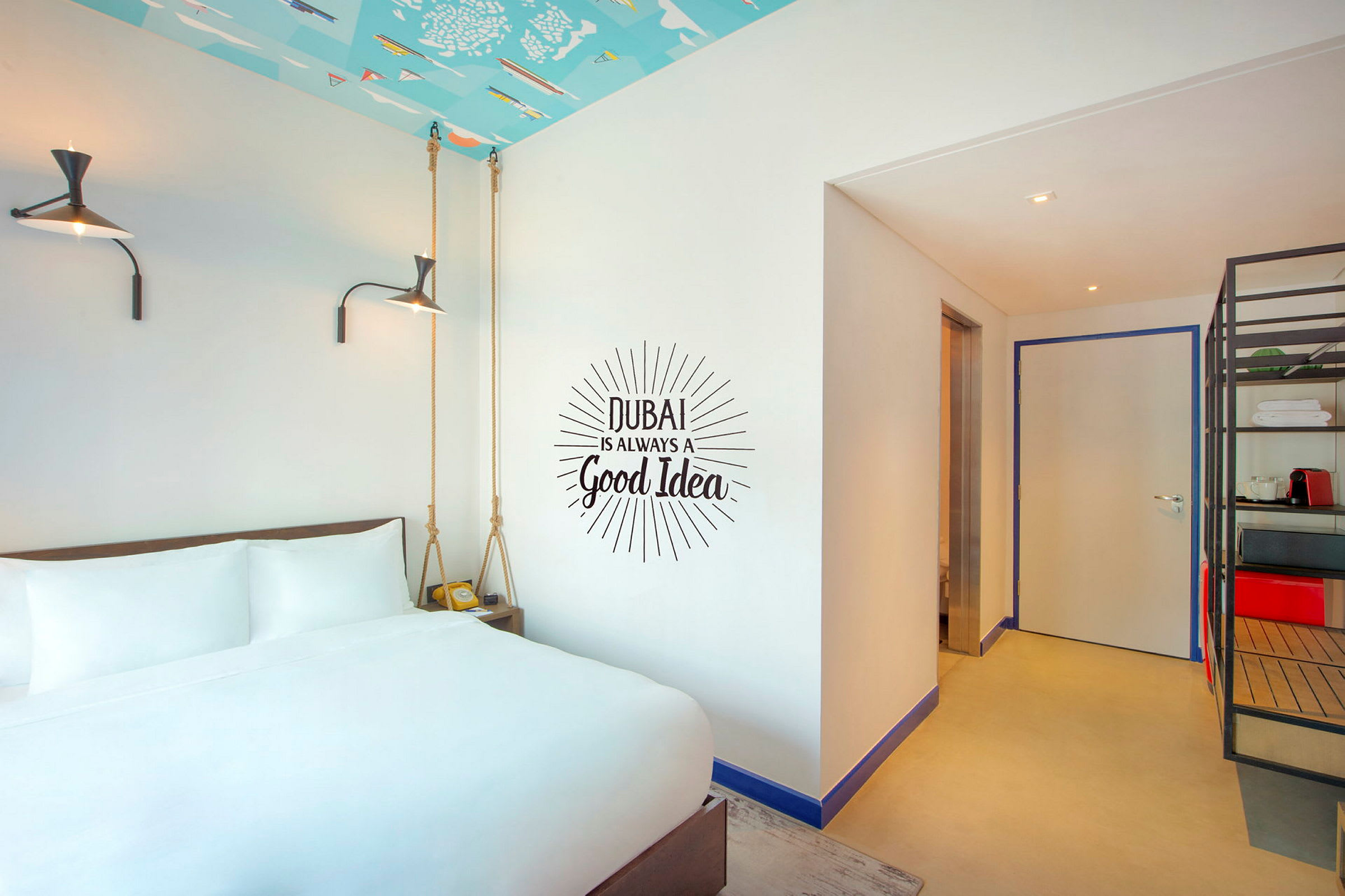Hotellrum med vit säng framför en vägg med texten "Dubai is always a good idea". (AI-genererad text)