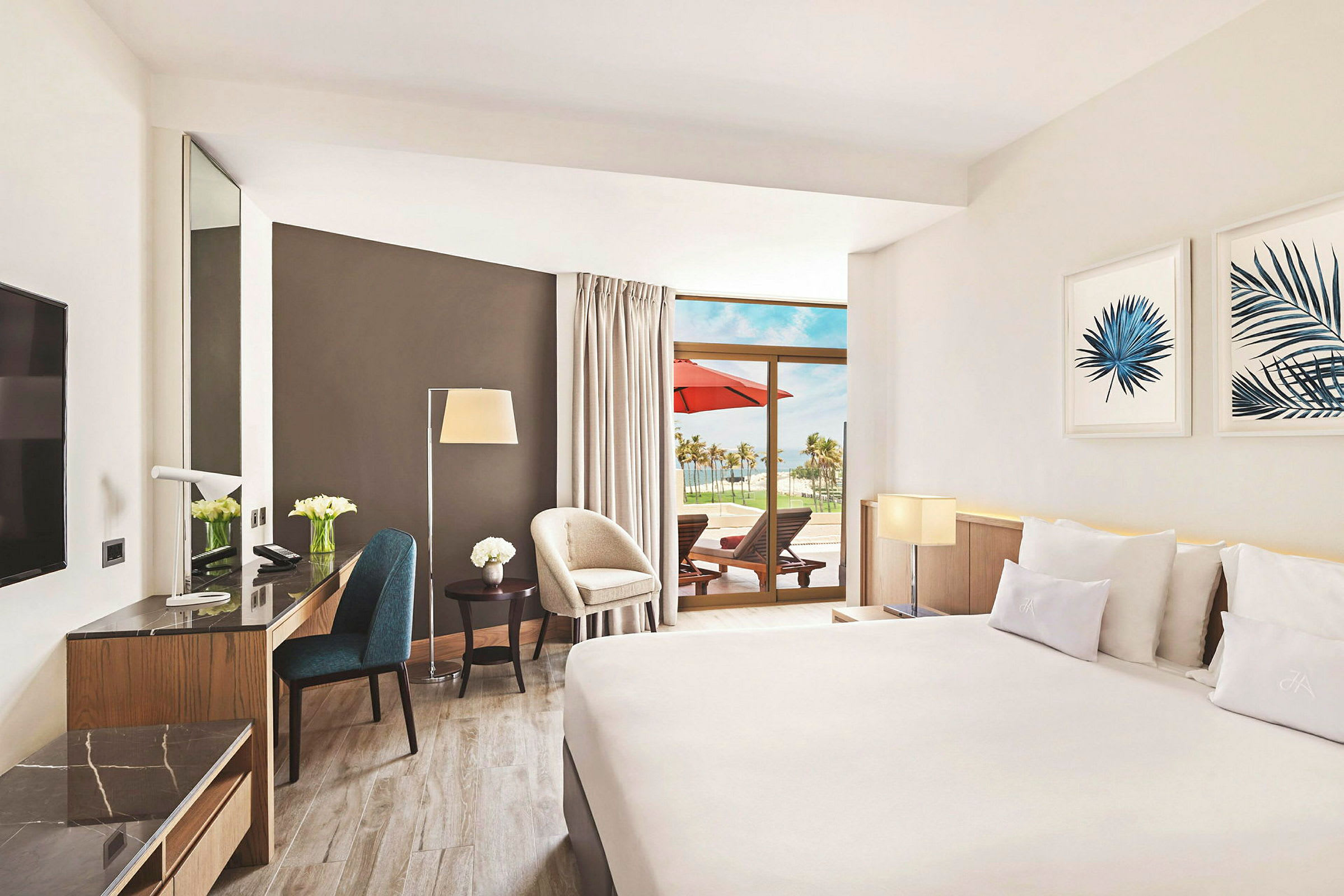 Ett hotellrum med moderna möbler, stor säng, marmorerat skrivbord och en terrass med solstolar och utsikt över palmer. (AI-genererad text)