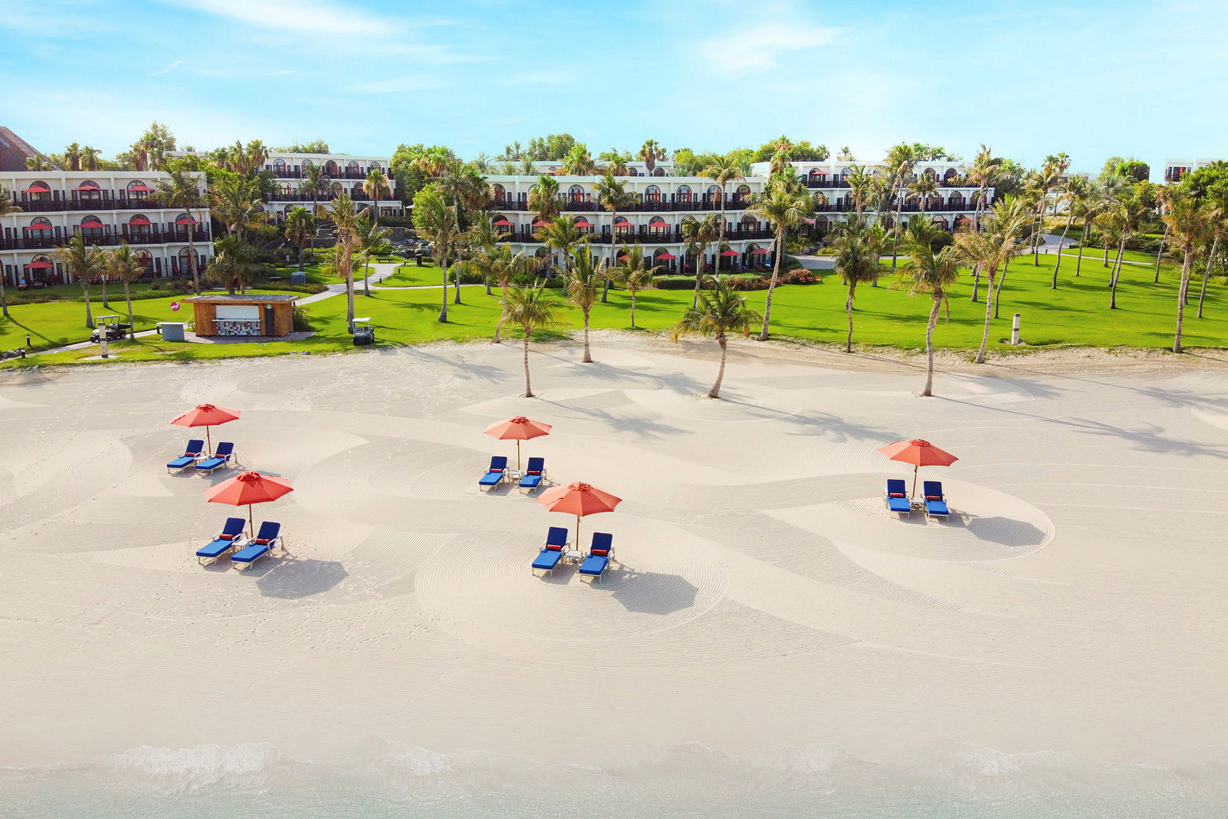 Bild av en strand med solstolar och parasoller framför en grönskande hotellträdgård. (AI-genererad text)