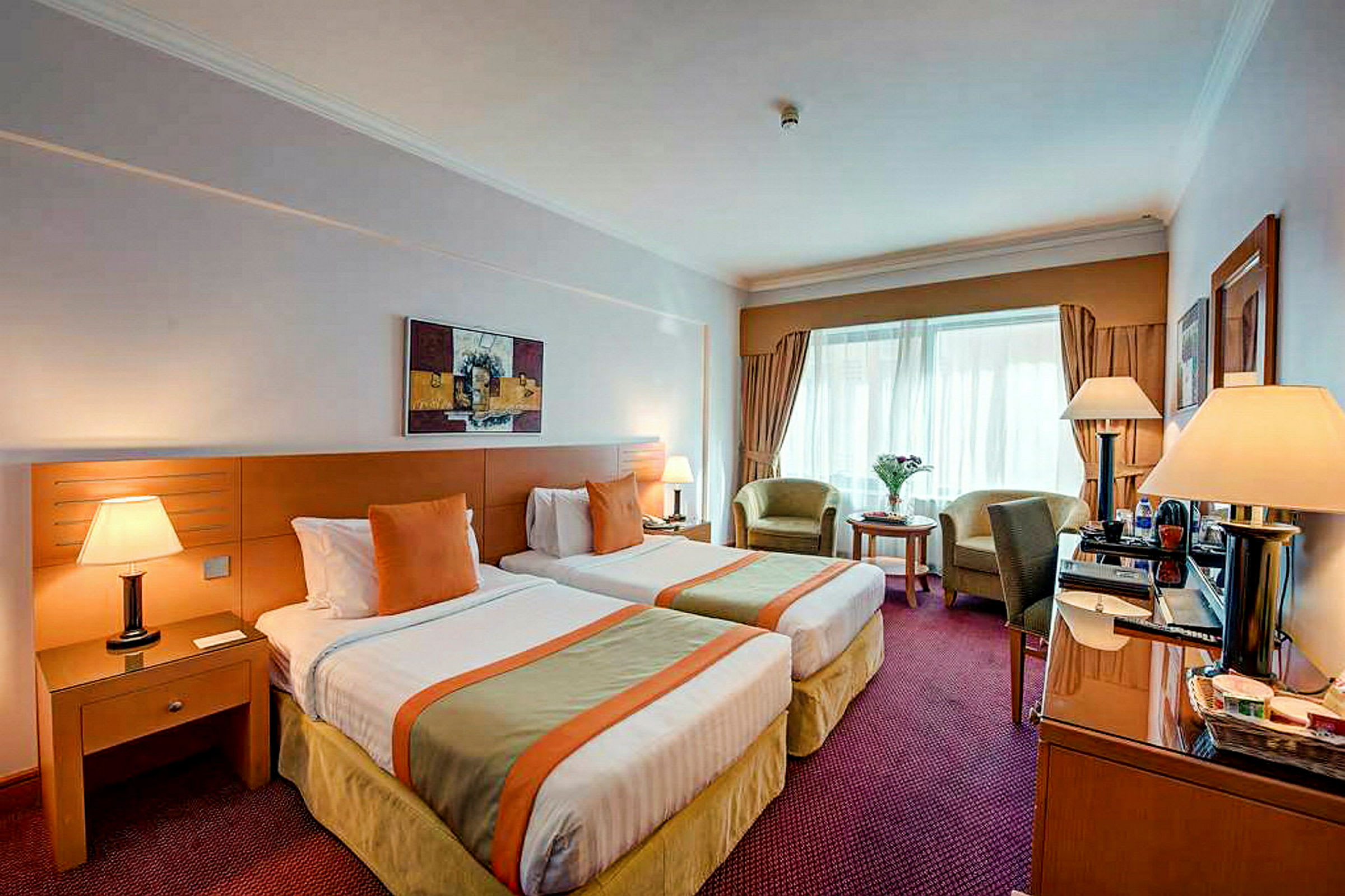 Ett hotellrum med två enkelsängar, bord, stolar och lampor. (AI-genererad text)