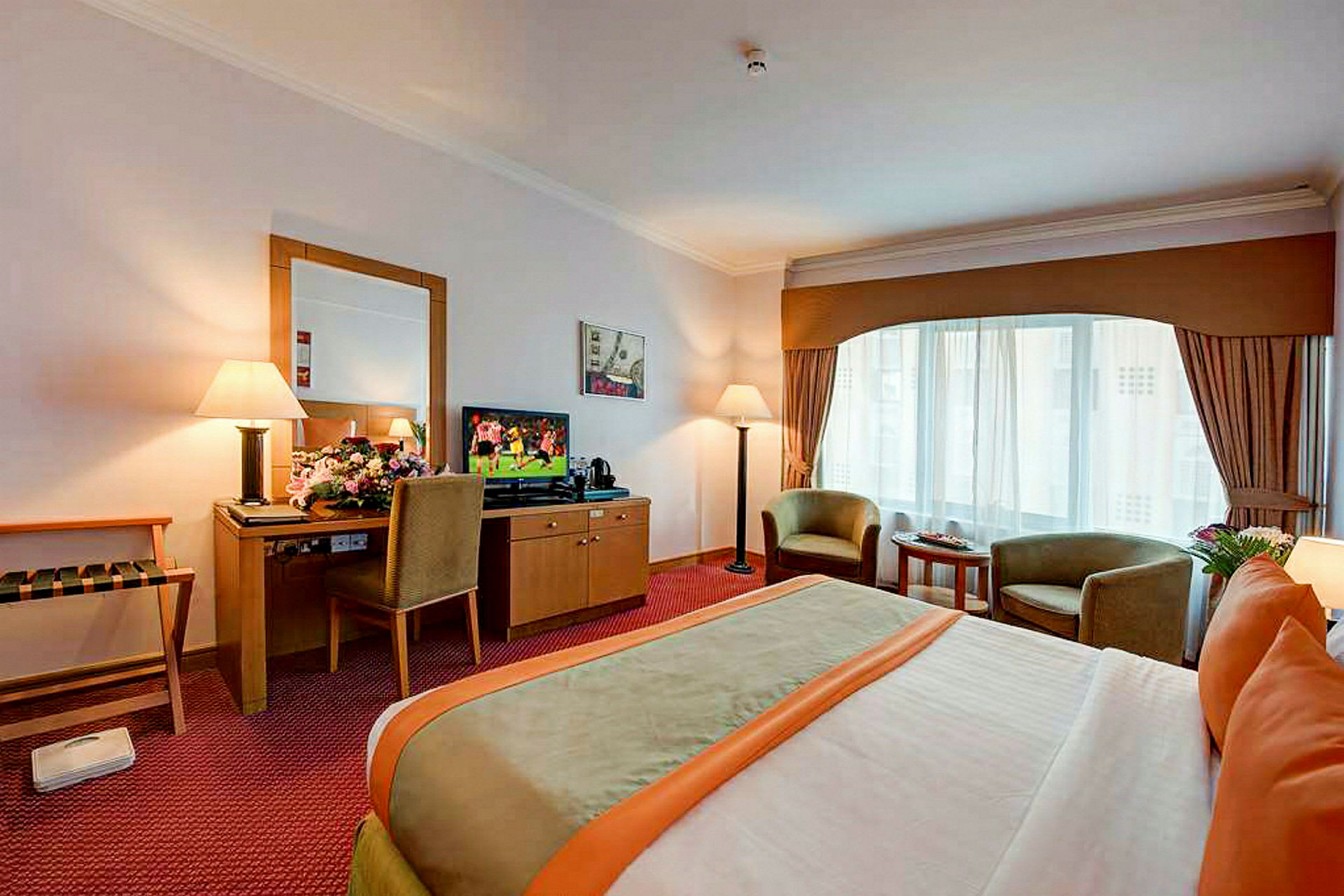 Ett hotellrum med en dubbelsäng, två fåtöljer framför ett stort fönster och en tv på en byrå bredvid ett skrivbord med en stol. (AI-genererad text)