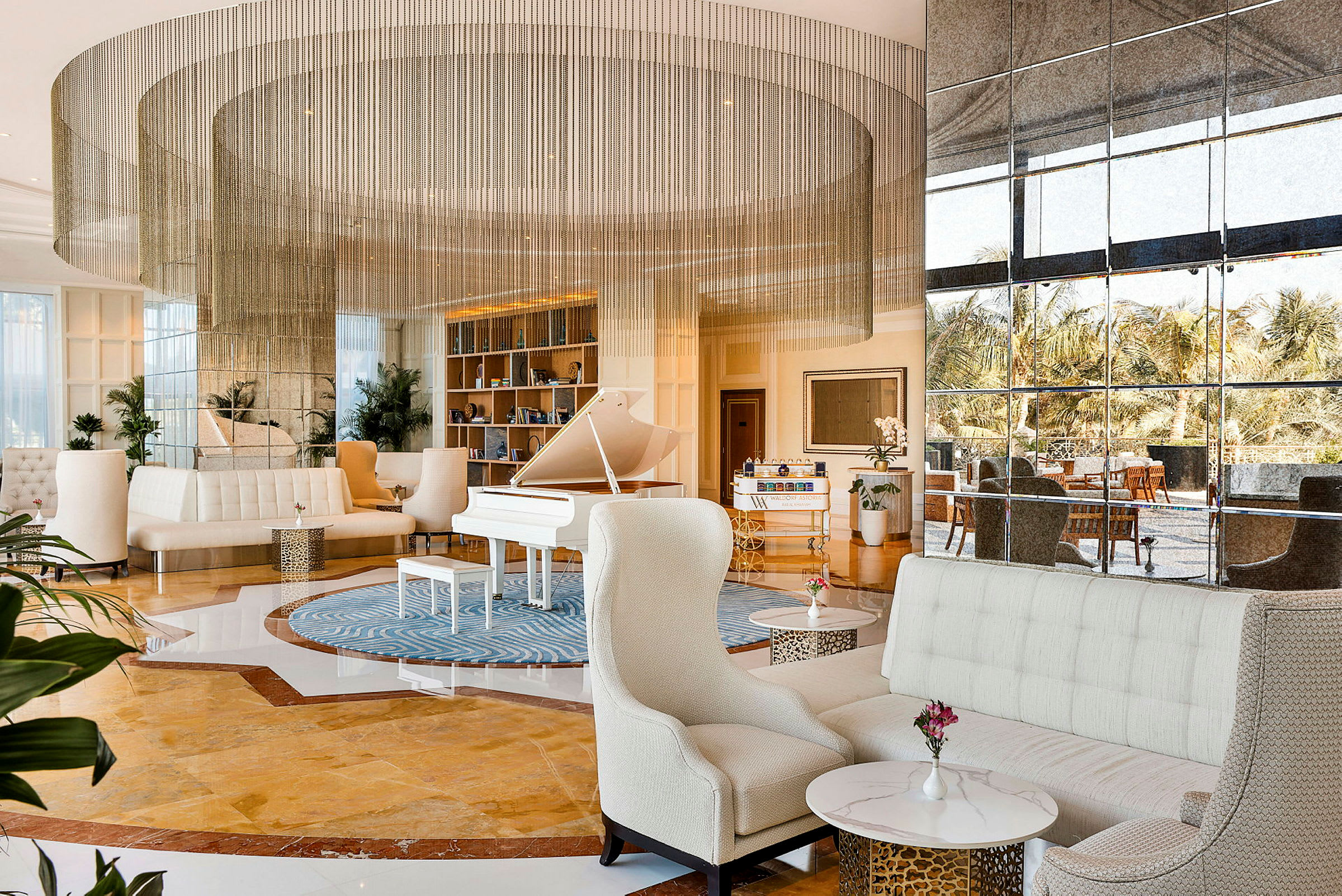 Ett elegant hotellounge-miljö med ett vitt piano, bekväma sittmöbler och stora fönster som vetter mot trädgården. (AI-genererad text)