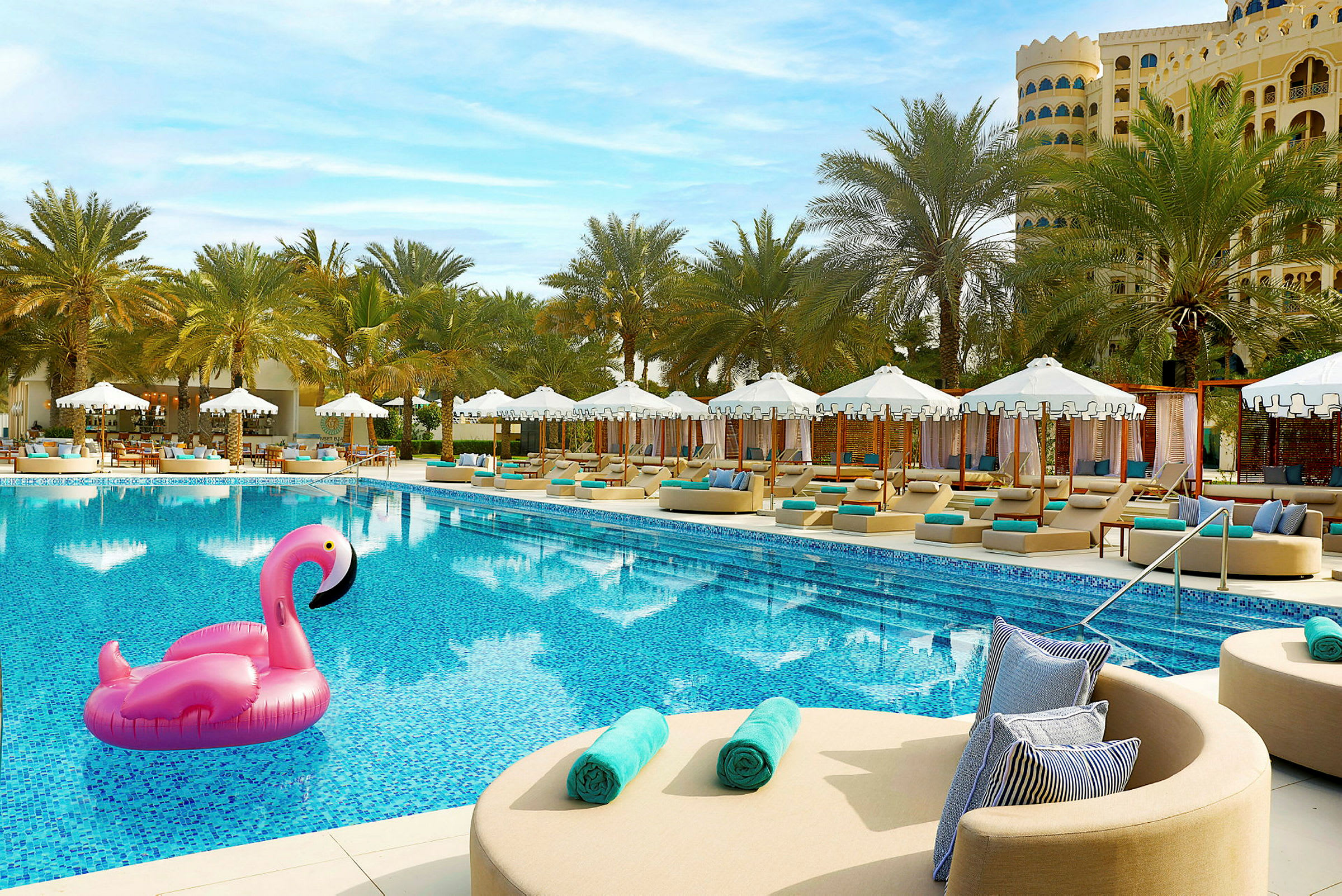 En pool omgiven av solsängar och parasoller med uppblåsbar flamingo i vattnet. (AI-genererad text)