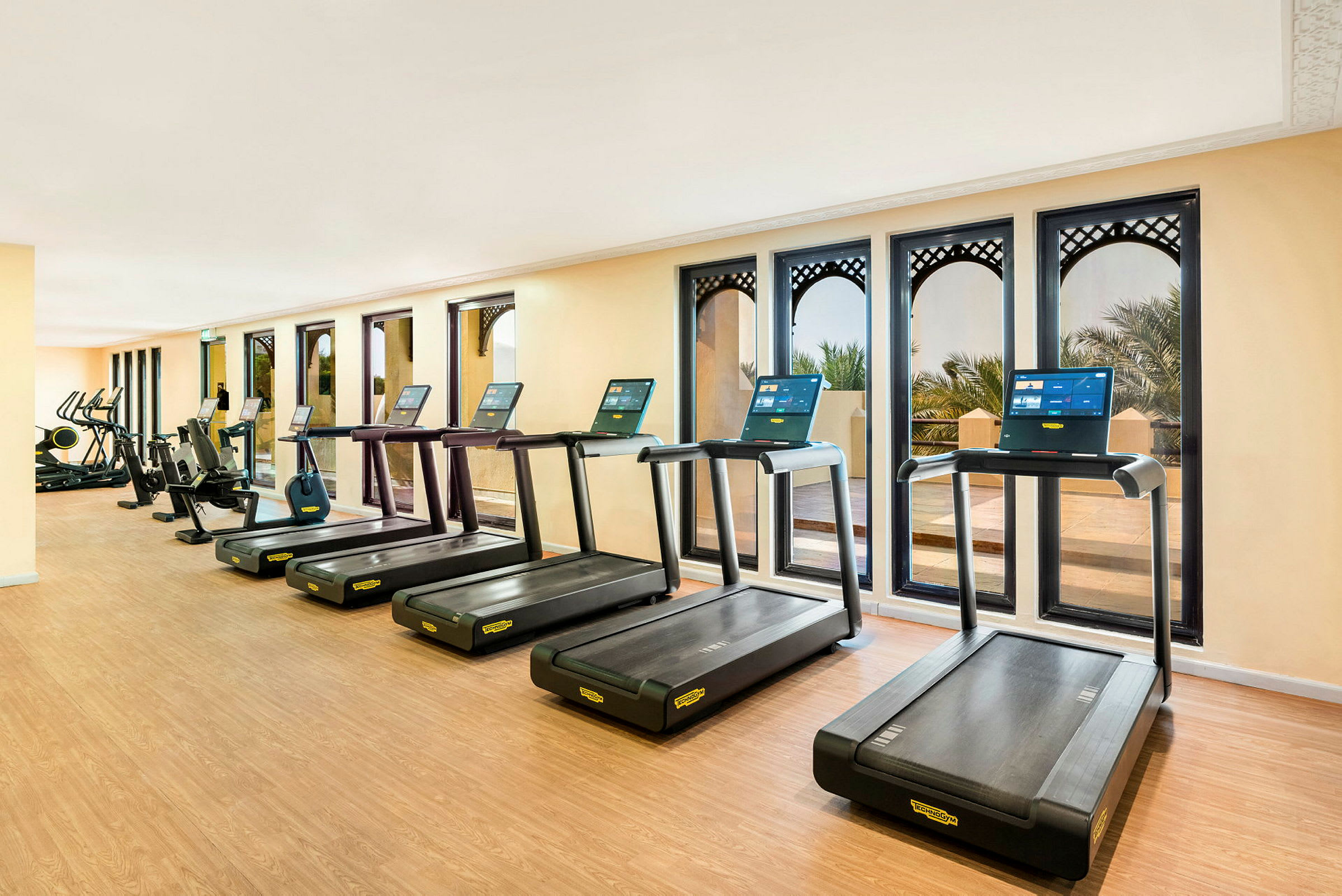 Ett gym med löpband och träningsmaskiner framför fönster. (AI-genererad text)