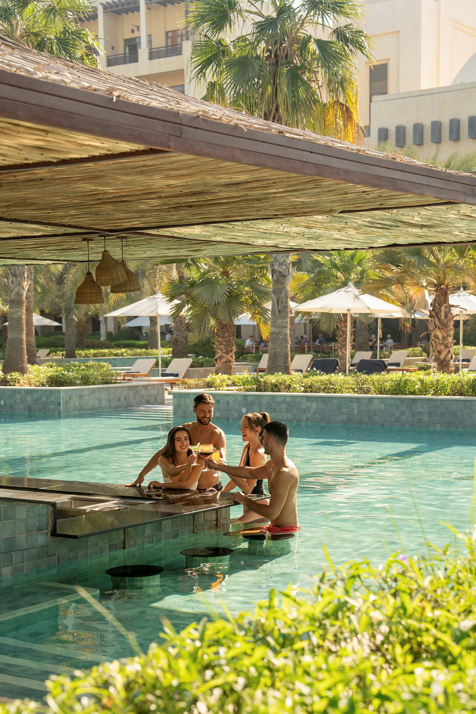 En pool bar där människor njuter av drinkar medan de sitter i vattnet, omgivna av solstolar och palmer. (AI-genererad text)