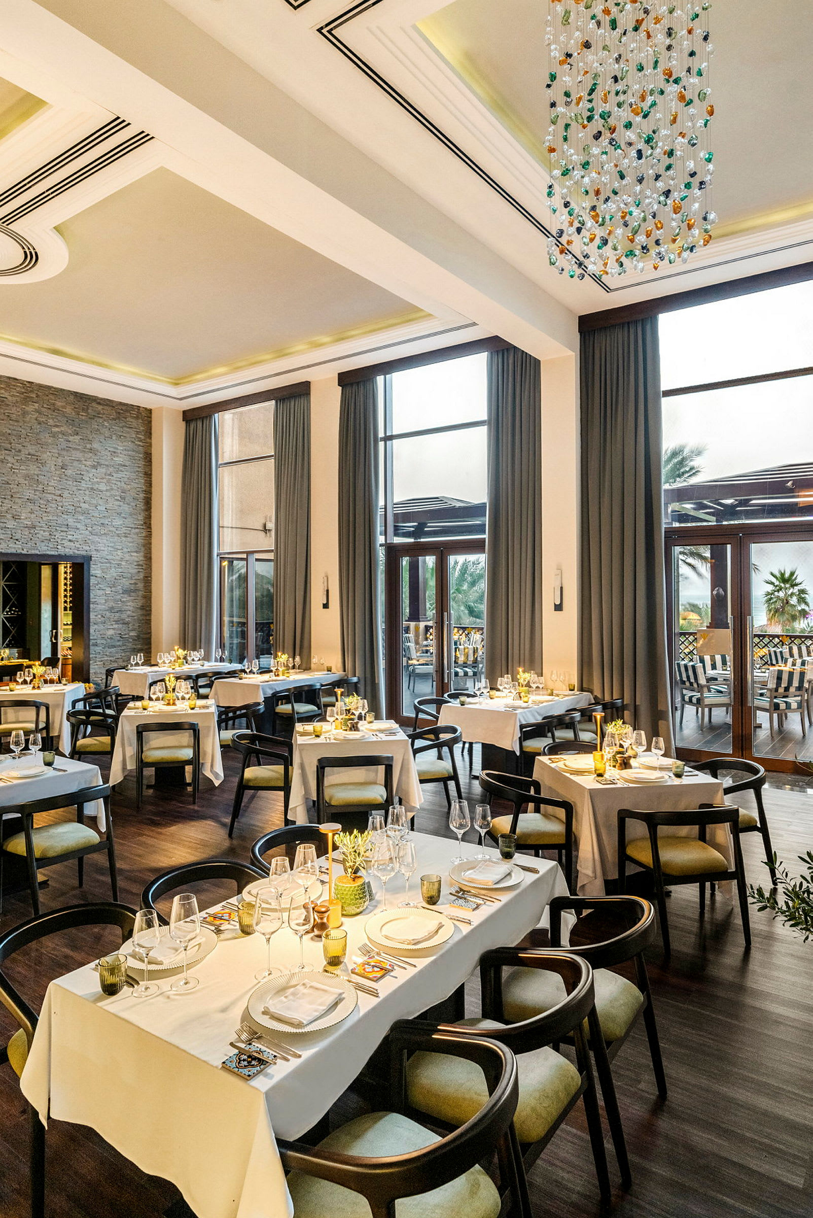 En elegant restaurang med dukade bord inför middag, stora fönster och en ljuskrona i taket. (AI-genererad text)
