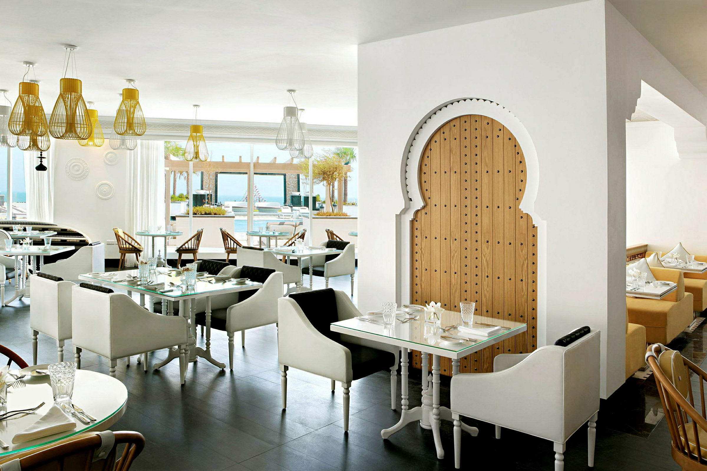 Interiör av en restaurang med modern och stilfull inredning. Ljusa sittplatser och belysning med en orientalisk träport. (AI-genererad text)