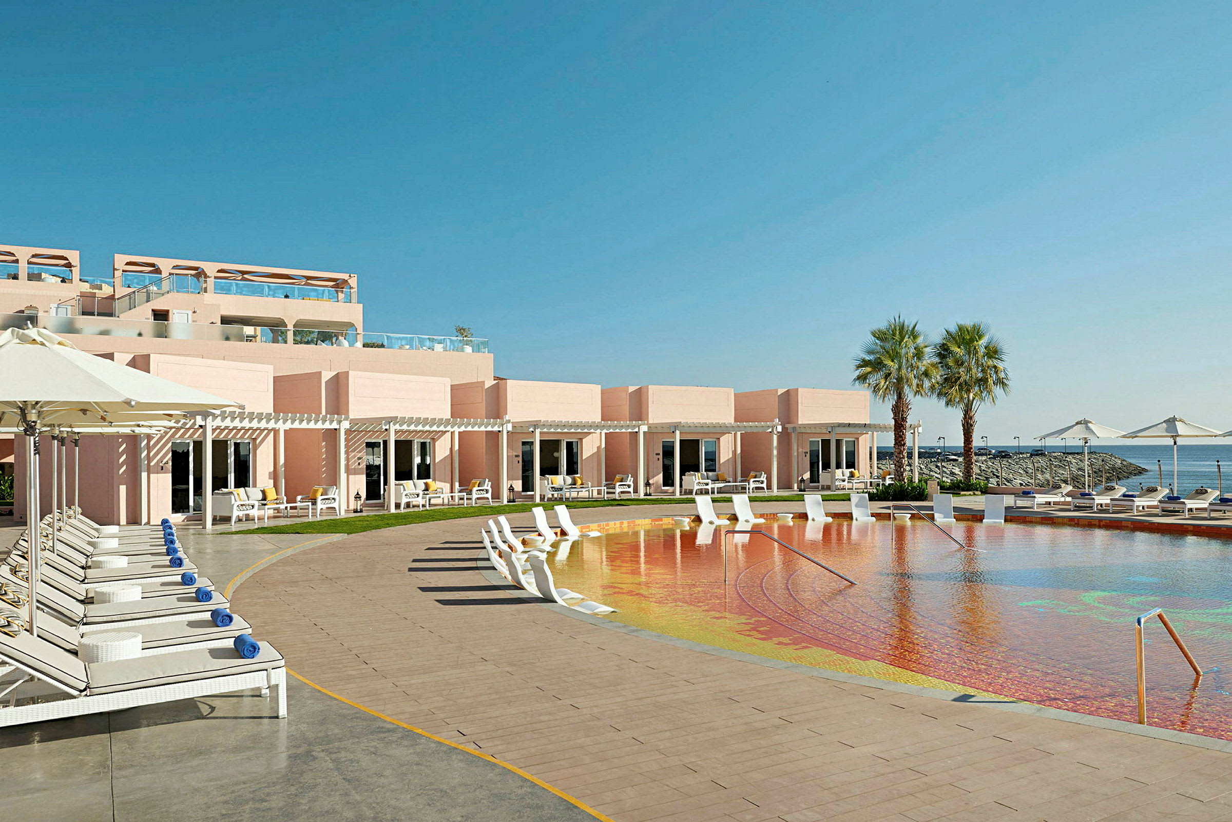Bild av ett hotellområde med pool, solstolar och palmer vid havet. (AI-genererad text)