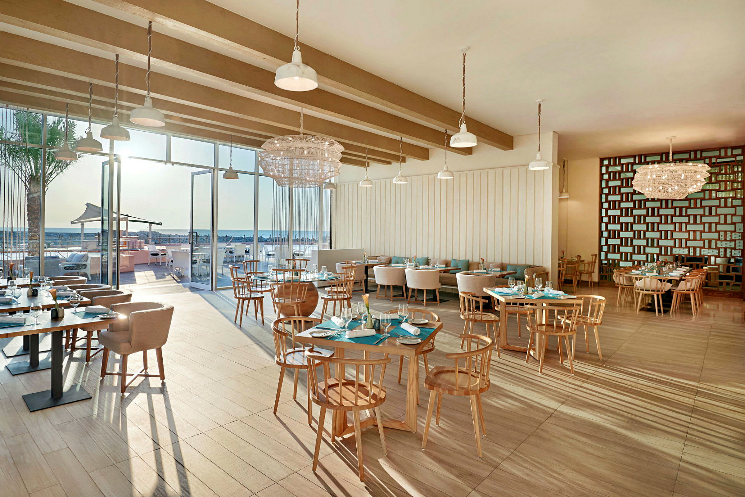 En modern restaurang inomhus med stora glasfönster som vetter mot en uteservering och stranden. (AI-genererad text)