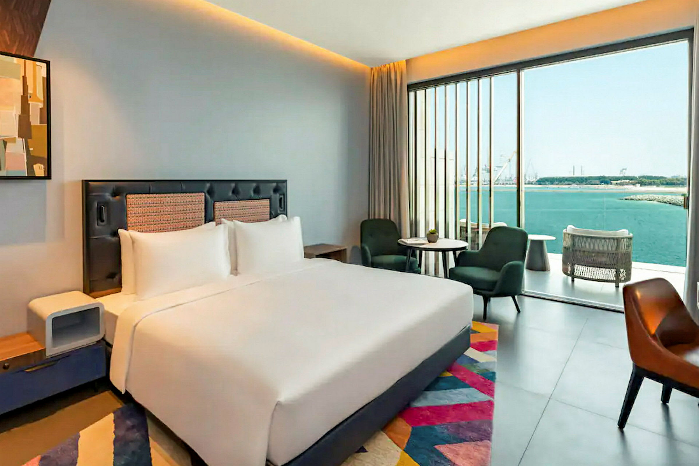 Ett modernt hotellrum med en stor säng, sittmöbler och ett stort fönster med utsikt över havet. (AI-genererad text)