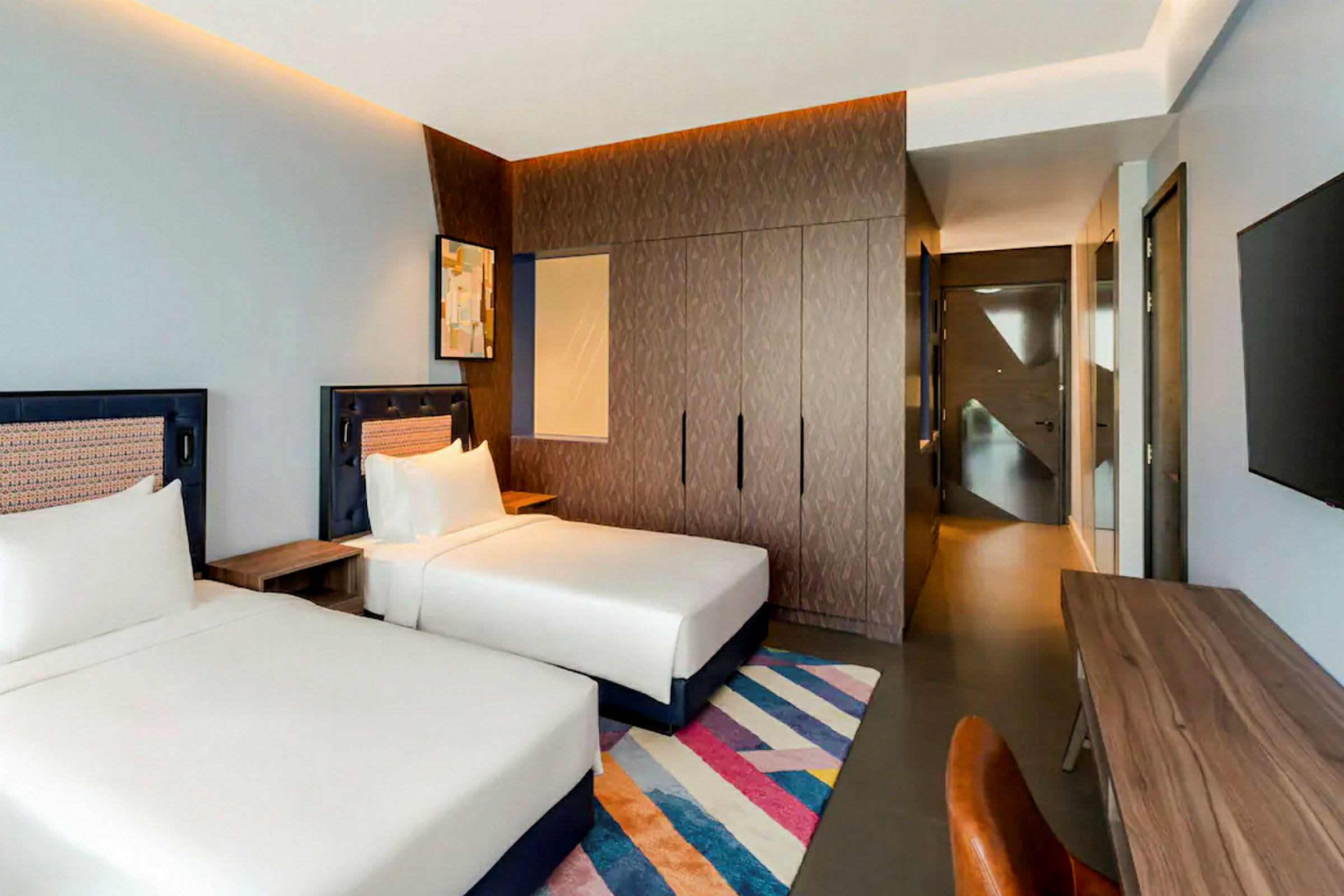 Ett hotellrum med två enkelsängar, ett skrivbord med stol, en garderob och en väggmonterad TV. (AI-genererad text)