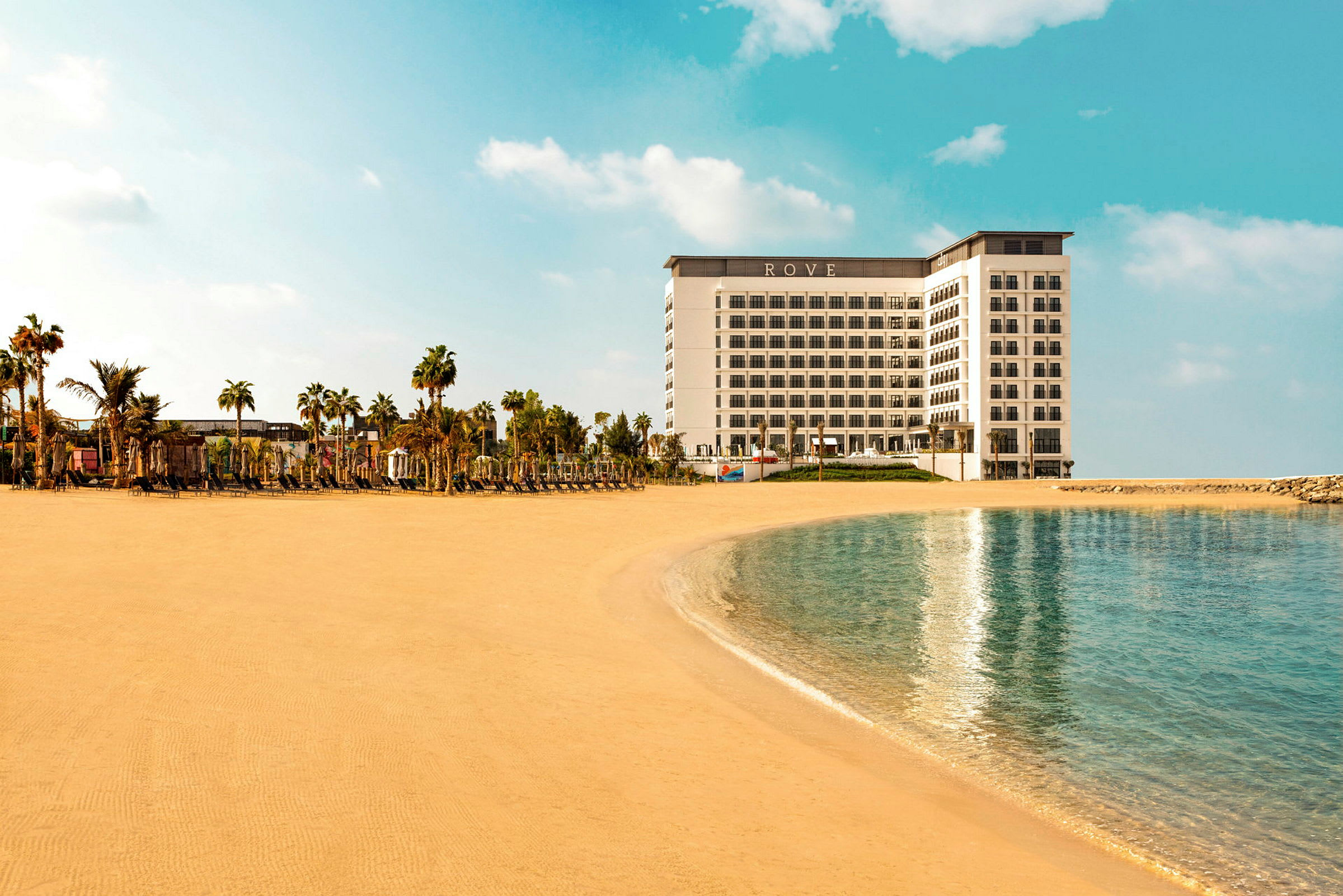 Hotellet Rove beläget vid en sandstrand och omgiven av palmer. (AI-genererad text)