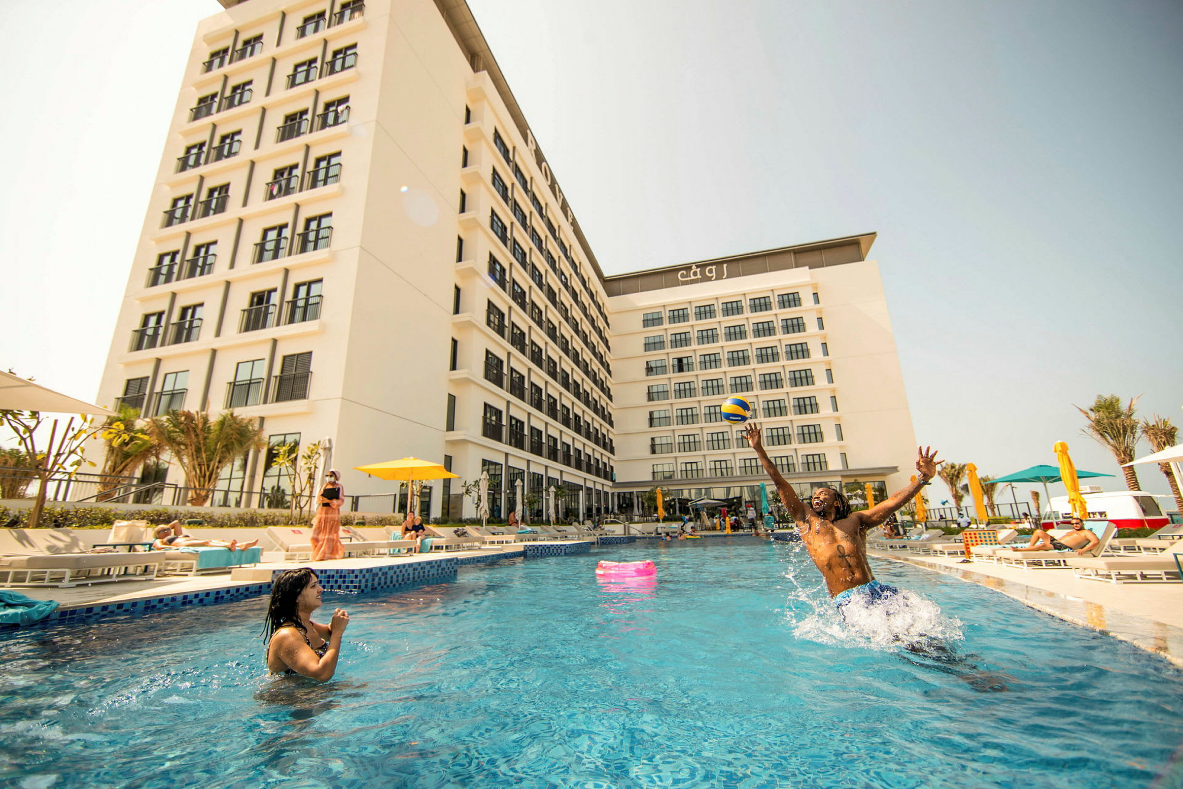 Ett hotell med vit fasad, omgiven av en pool och solstolar. (AI-genererad text)