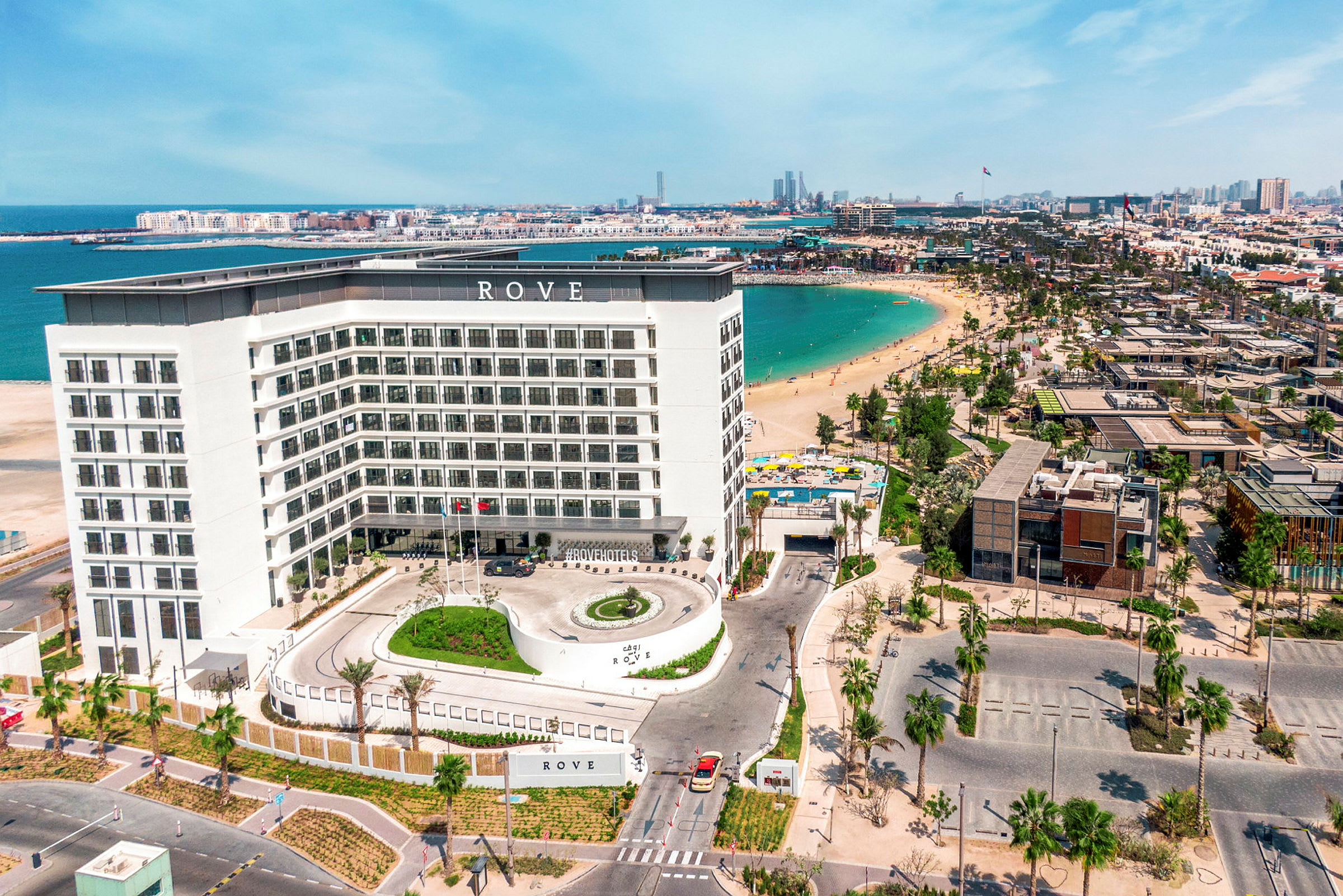 Ett hotell med en vit fasad vid en strand med blått vatten. (AI-genererad text)