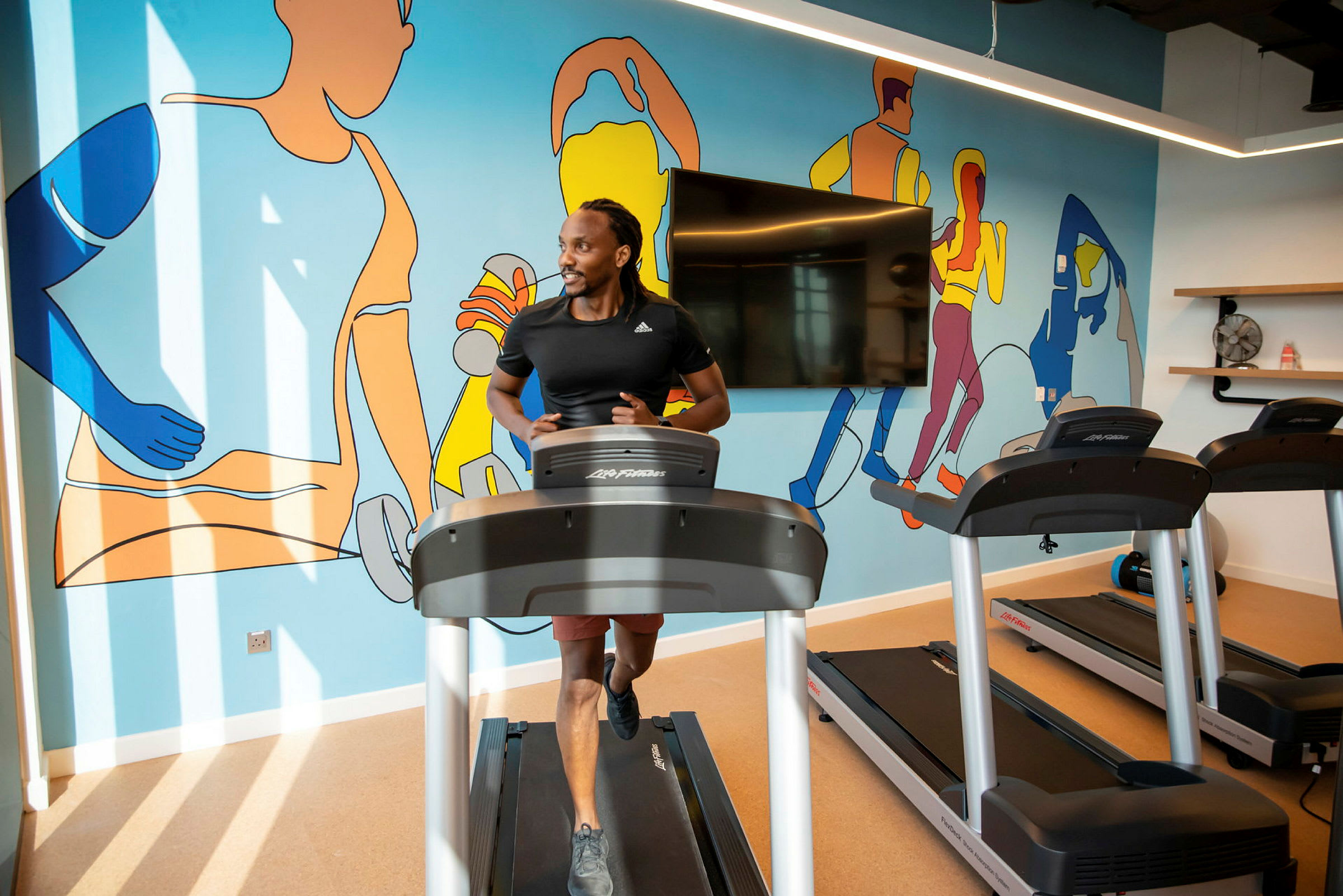 Person springer på ett löpband i ett gym med färgglad väggkonst. (AI-genererad text)