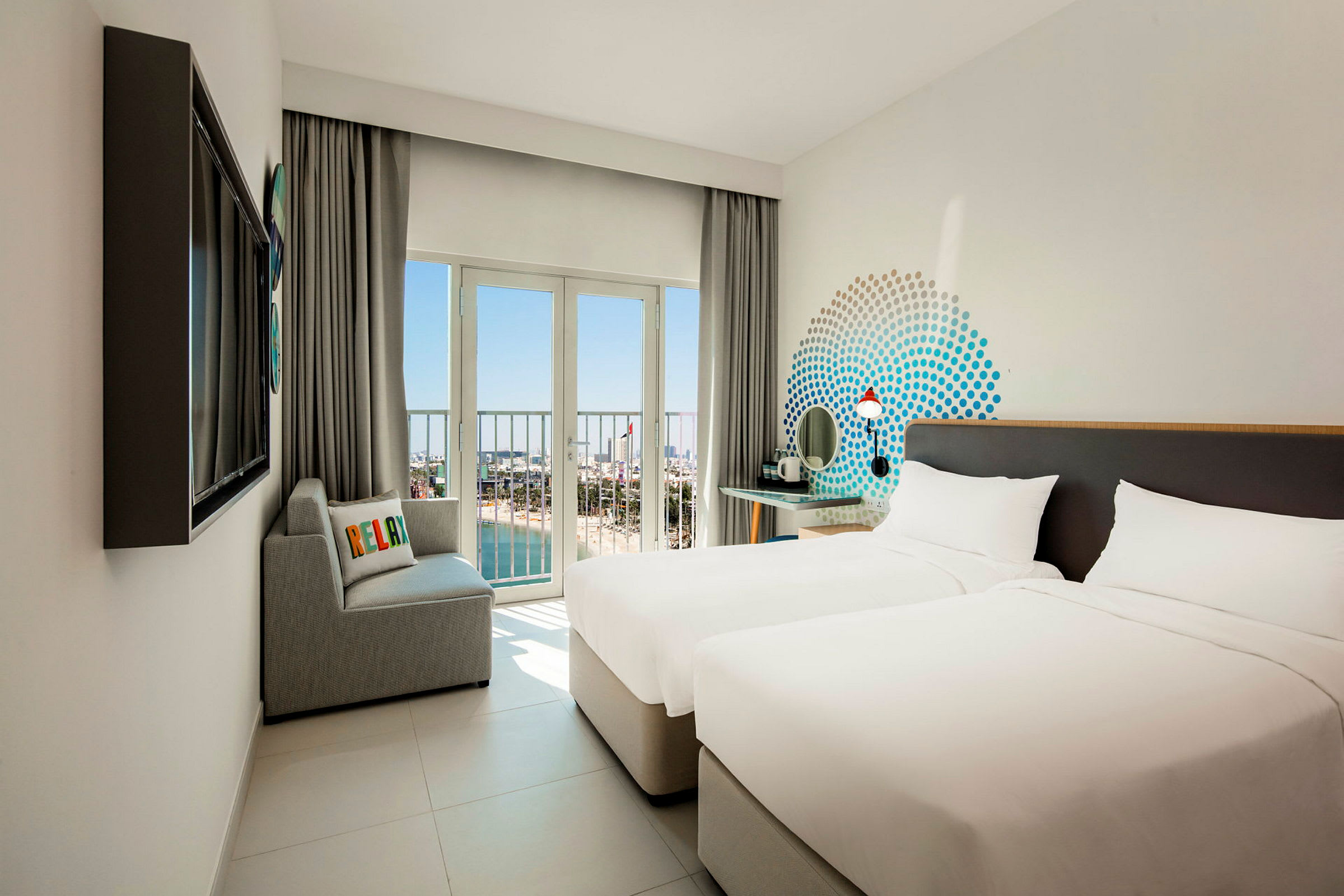 Hotellrum med två enkelsängar, en soffa och utsikt genom stora fönster mot stranden och havet. (AI-genererad text)