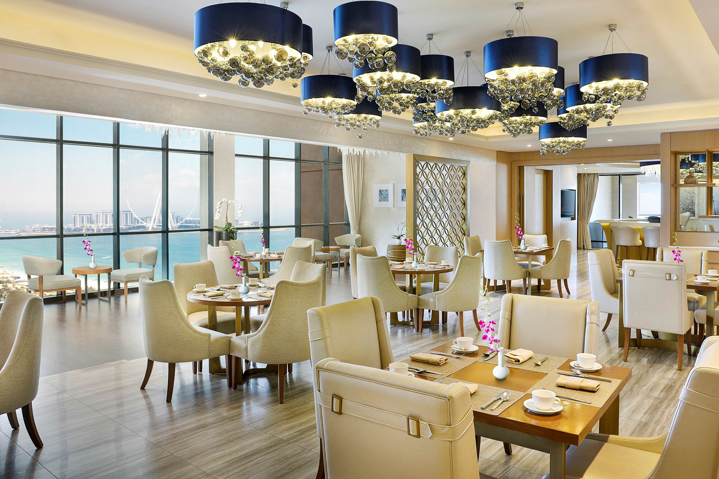 Interiör av en elegant restaurang med havsutsikt, ljusa möbler och dekorativa ljuskronor. (AI-genererad text)